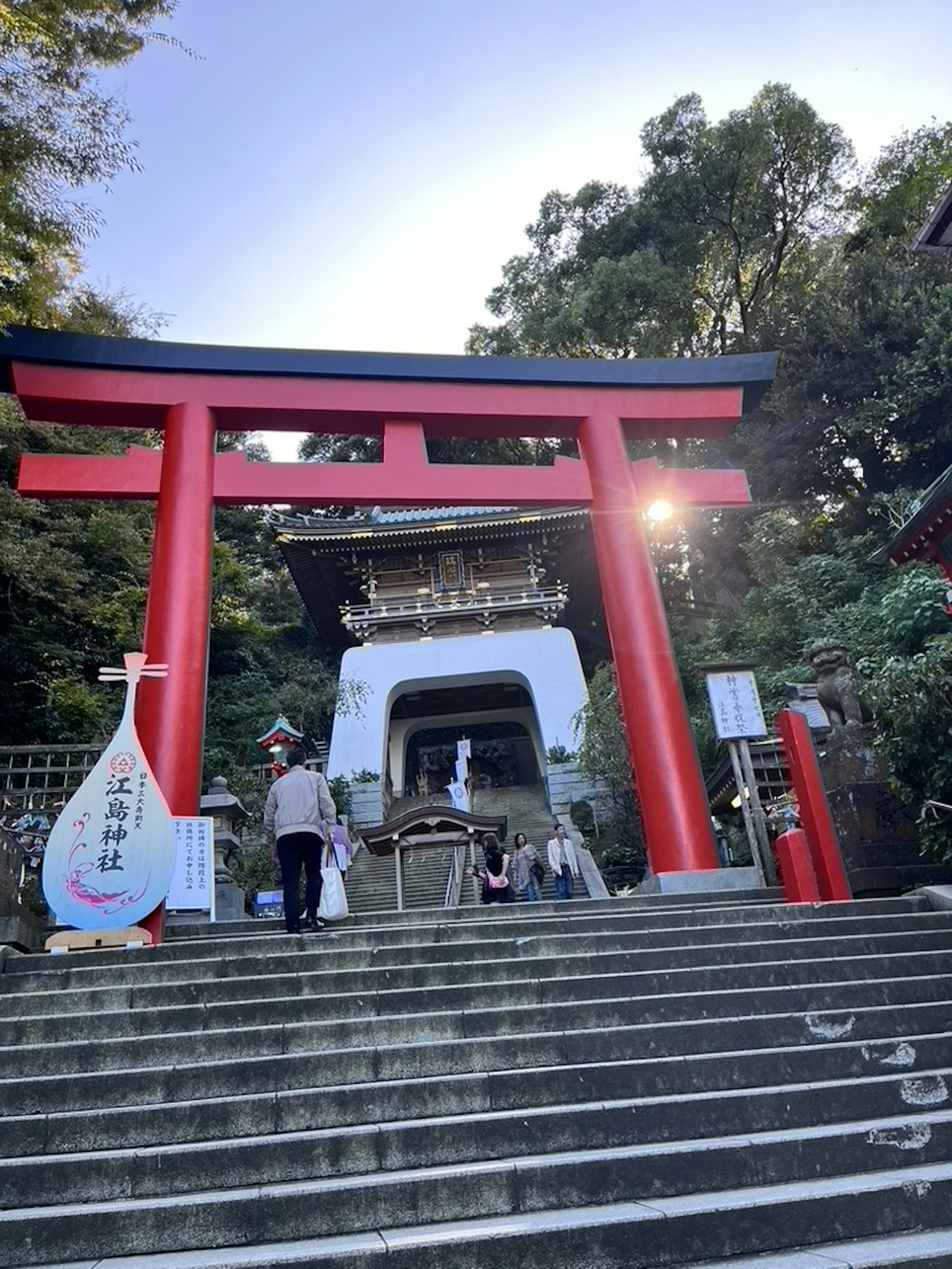 Puerta torii roja y escaleras del santuario con visitantes y fondo natural sereno