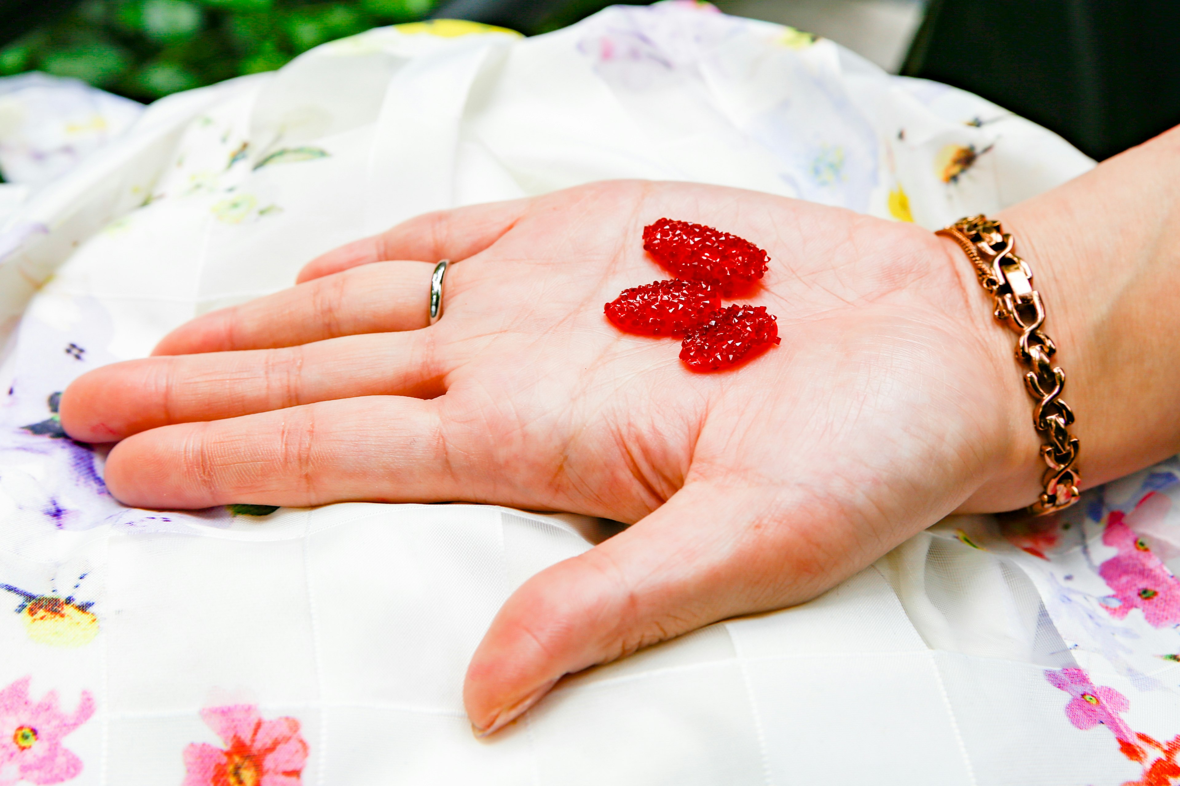 Drei rote Bonbons auf einer offenen Handfläche mit floralem Hintergrund