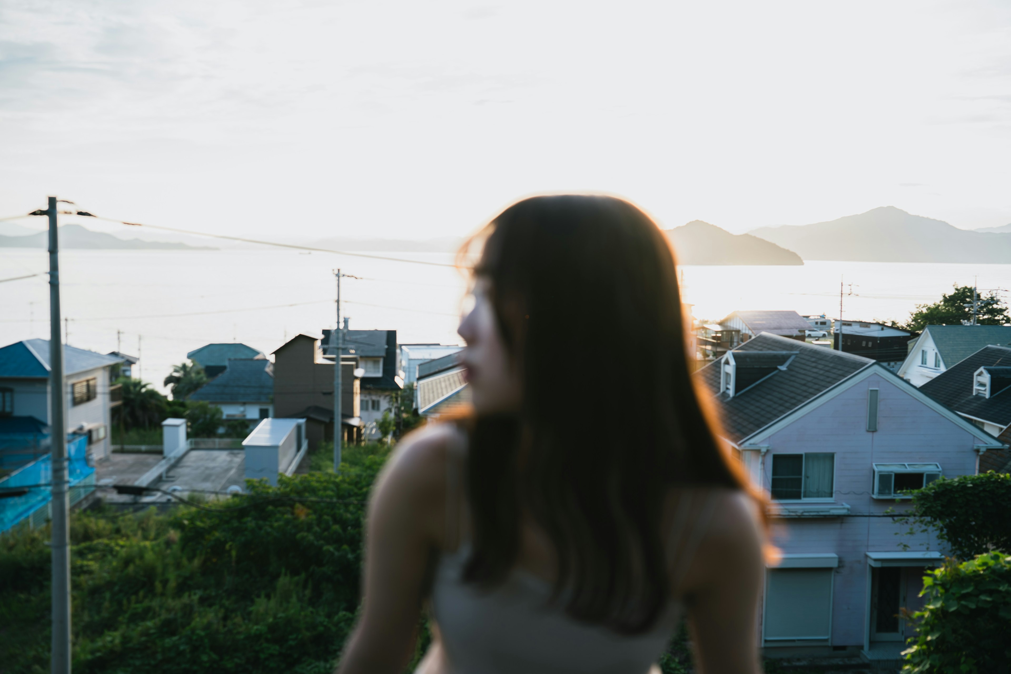 夕日を背にした女性が家々を見渡す風景