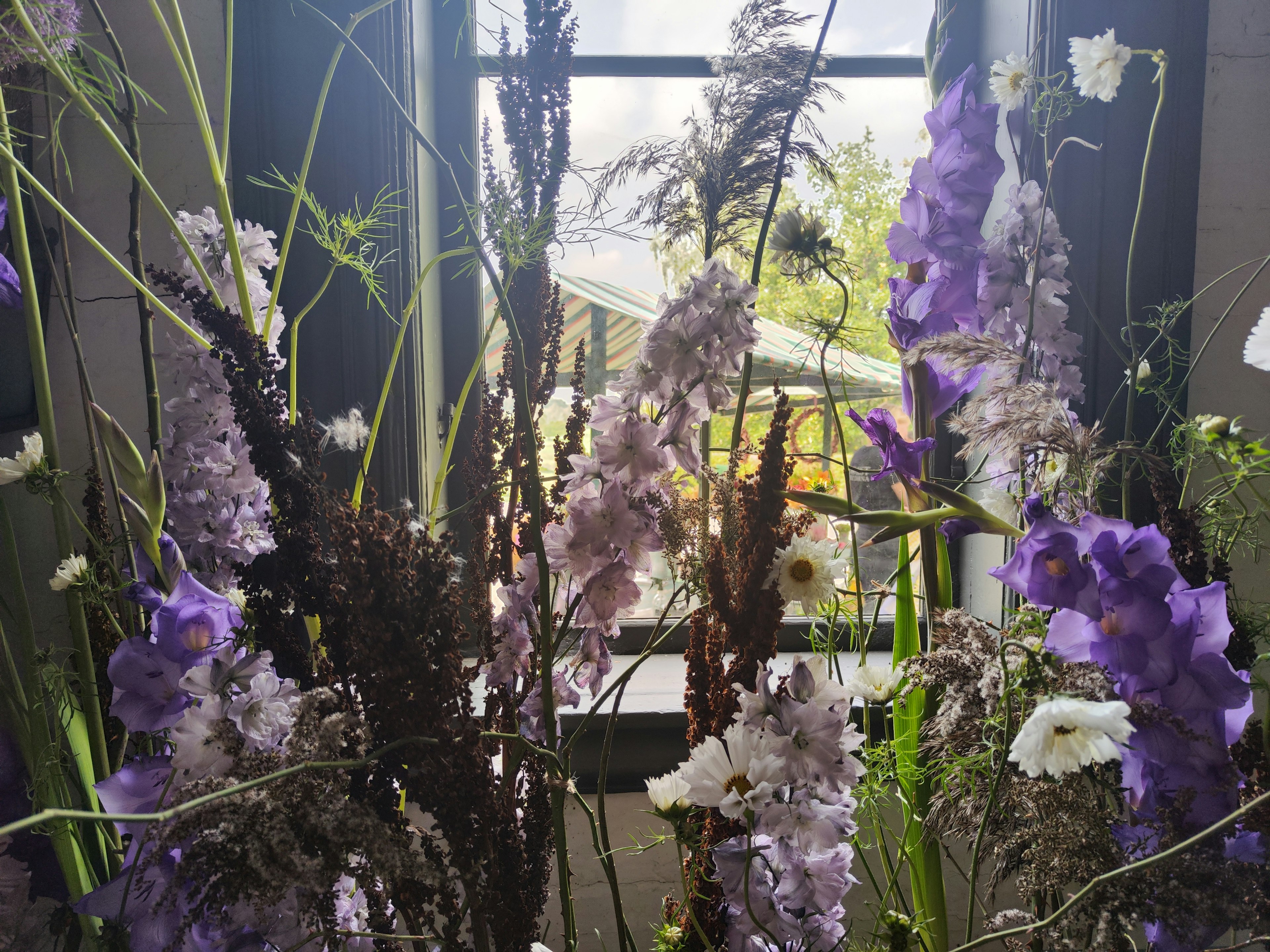 Un arreglo floral con flores moradas y blancas frente a una ventana