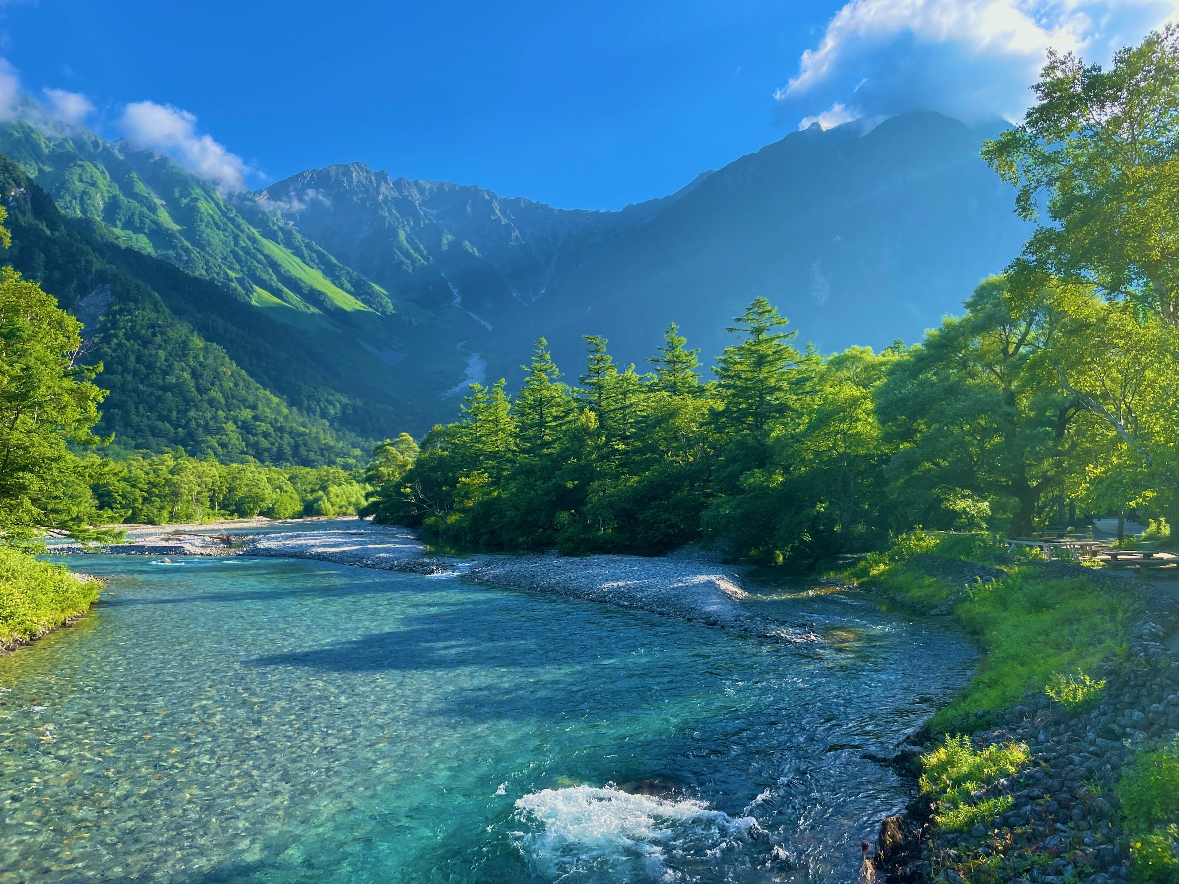 Vista panoramica di un fiume limpido circondato da montagne alberi verdi rigogliosi e cielo blu brillante