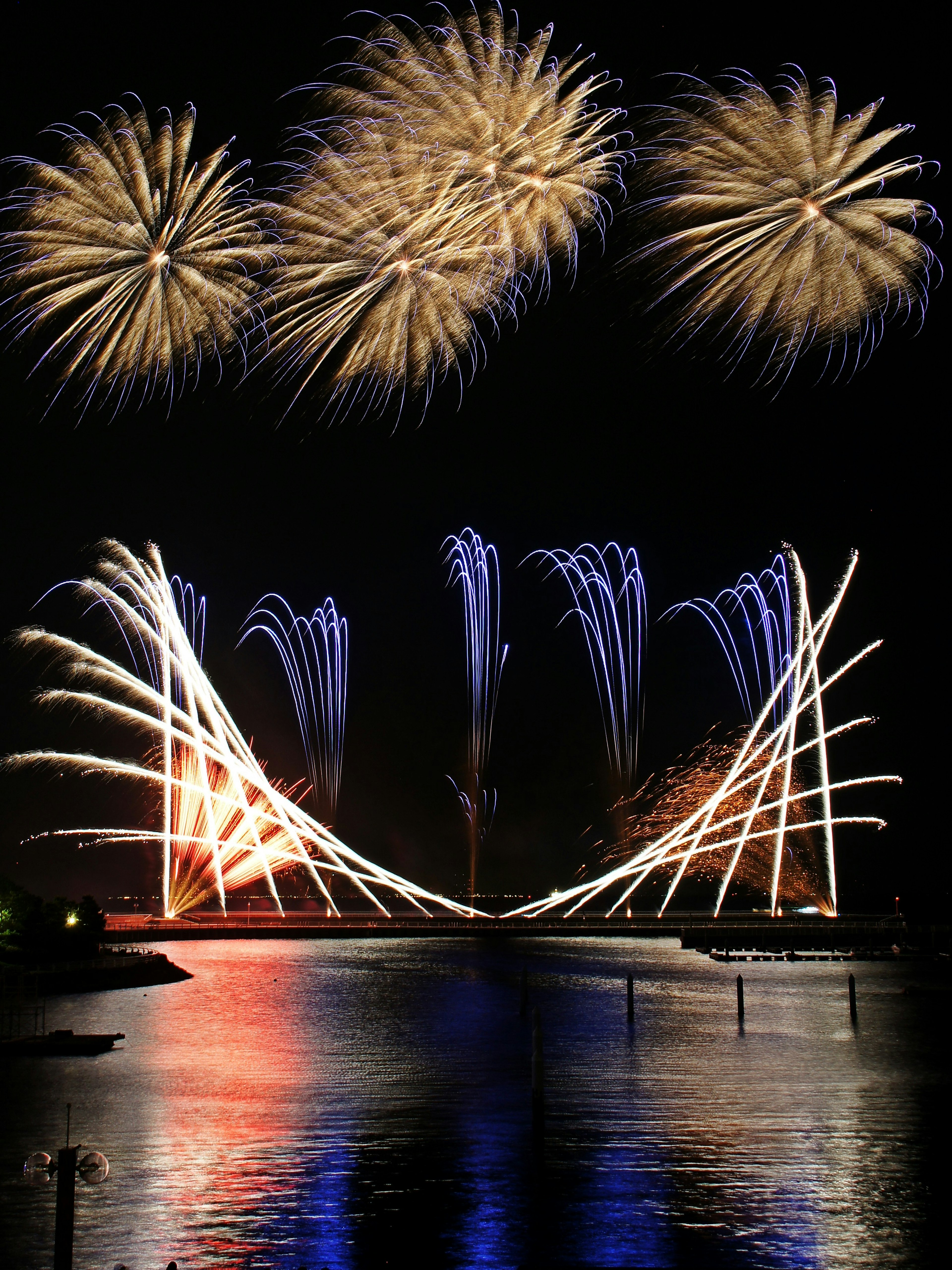 Espectáculo de fuegos artificiales coloridos sobre un cuerpo de agua con reflejos por la noche