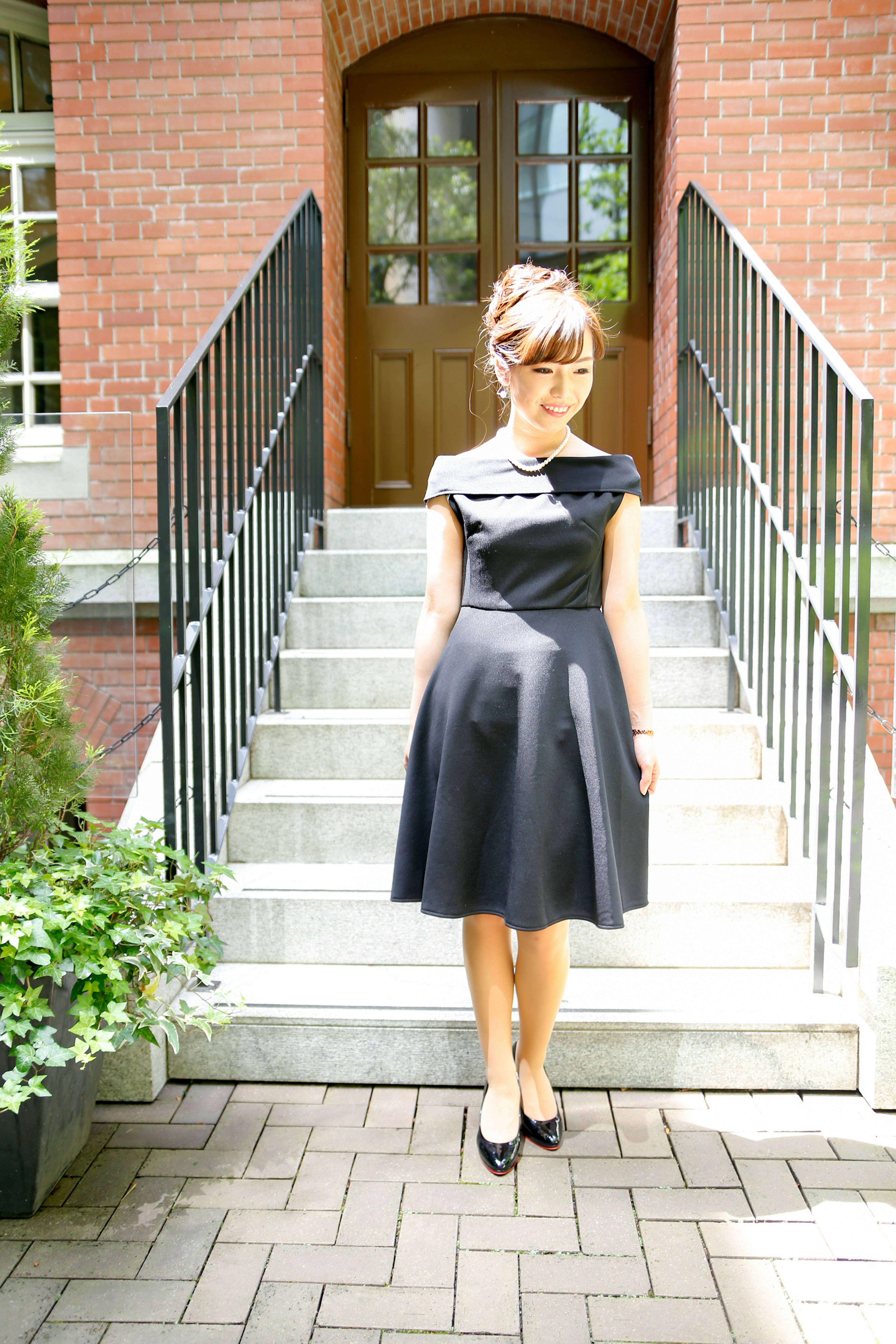 A woman in a black dress standing on stairs in front of a brick building