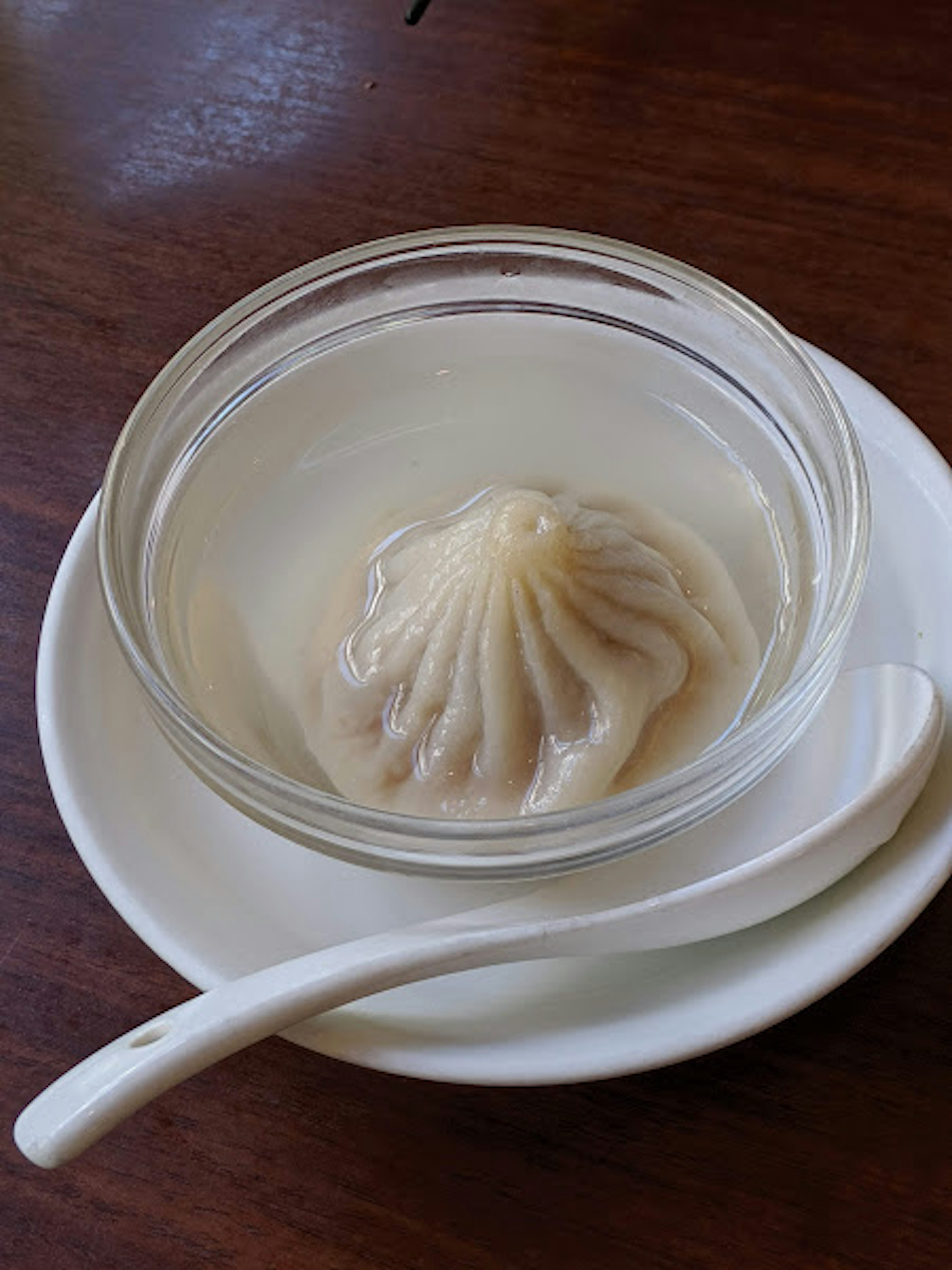 Steamed dumpling served in a clear bowl with a spoon