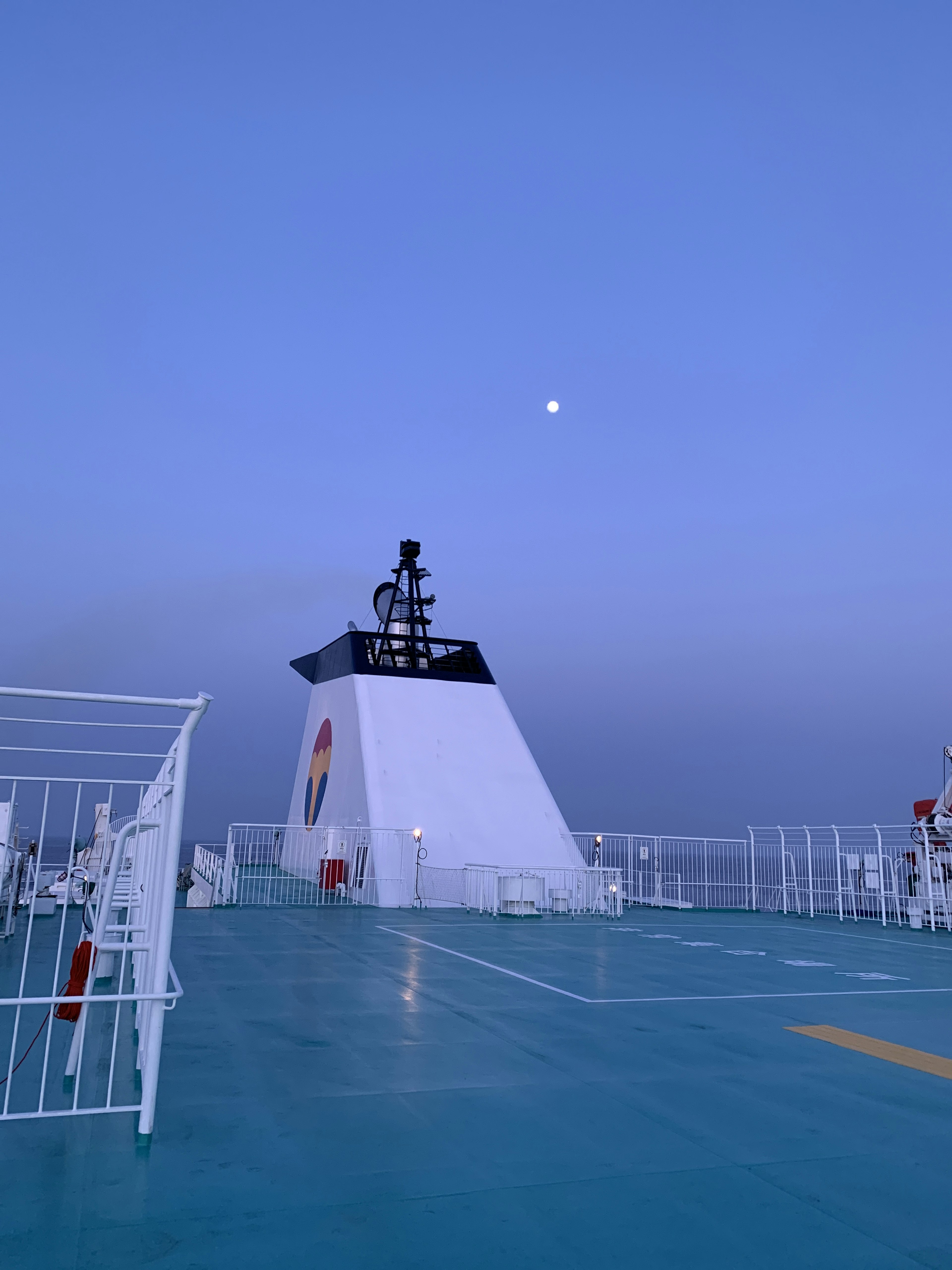 Cubierta de barco bajo un cielo azul con una torre y la luna