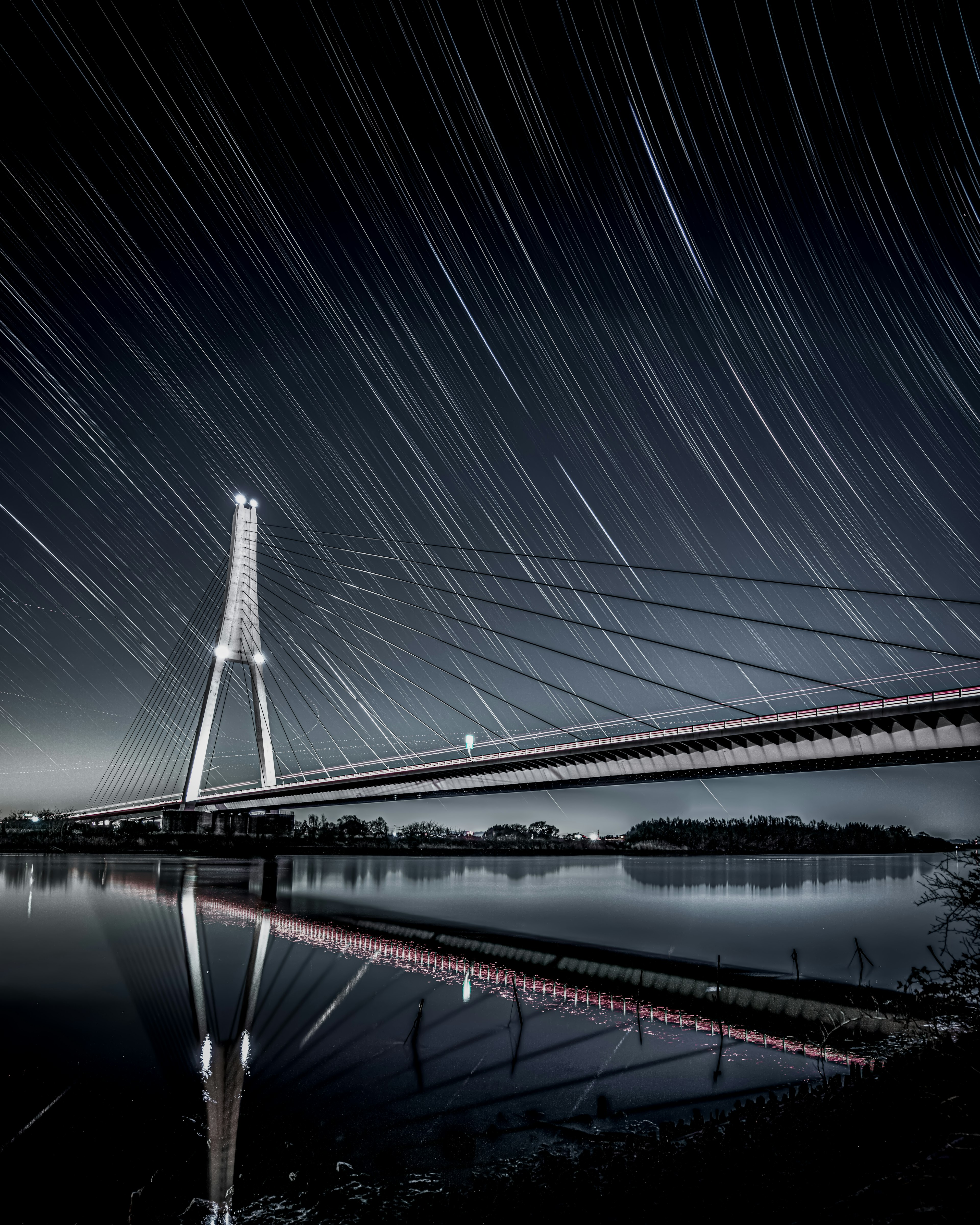 Pemandangan dengan jejak bintang di langit malam dan refleksi indah dari jembatan