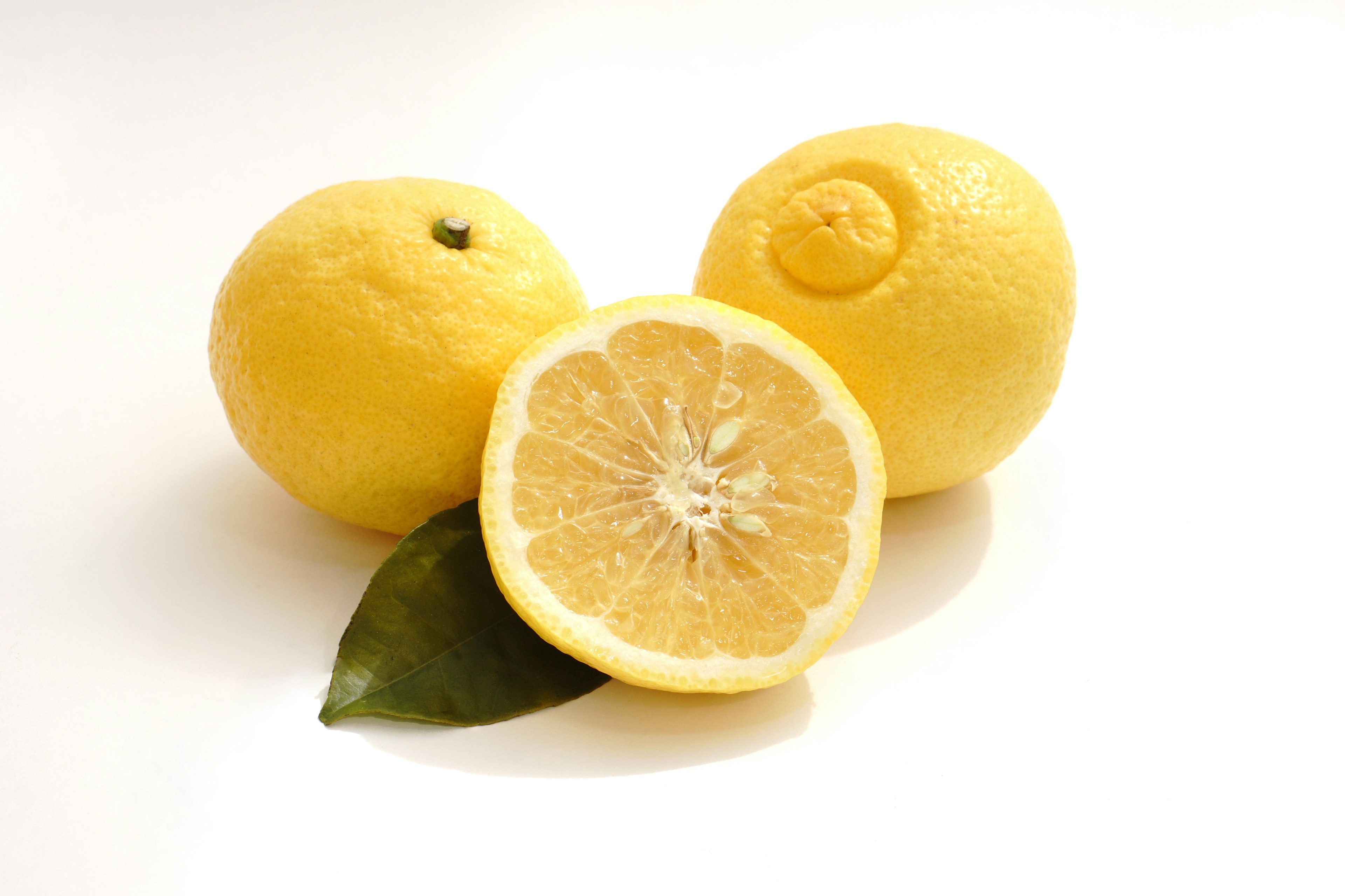 Tre limoni gialli con un limone affettato e una foglia verde