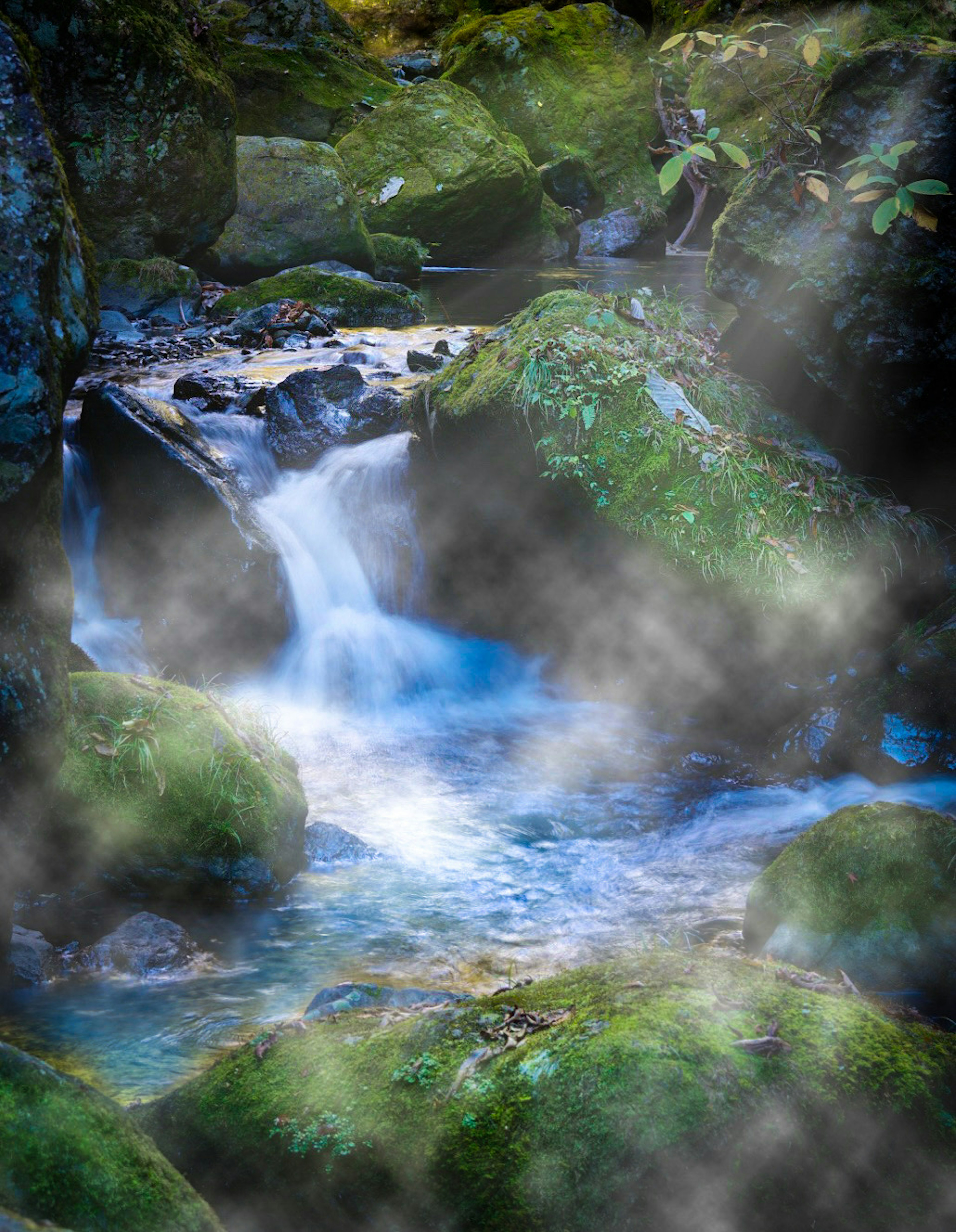 Ein Bach, der über moosbedeckte Felsen fließt, mit einer nebligen Atmosphäre