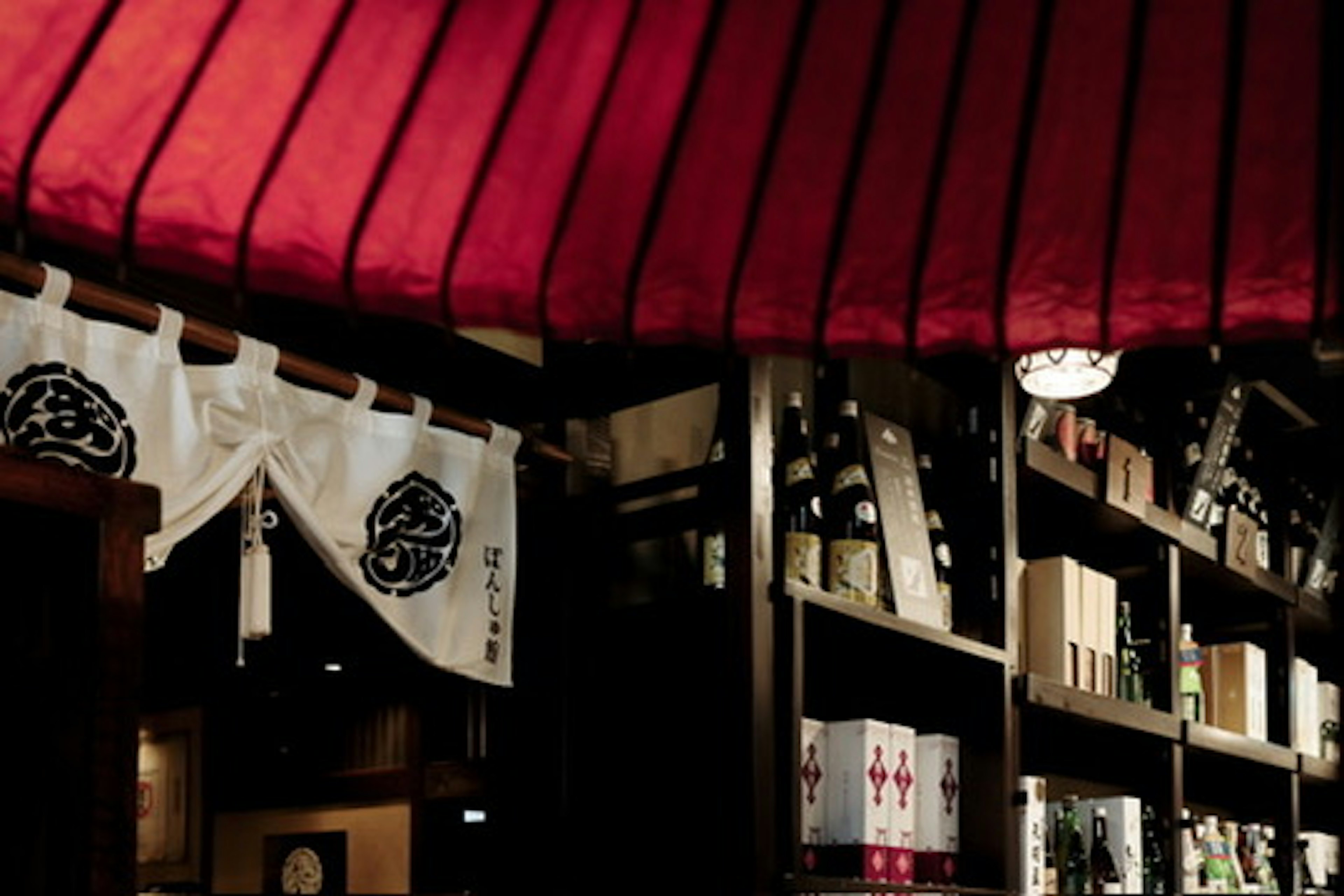 Interior de un izakaya con un techo rojo y estantes de botellas de sake