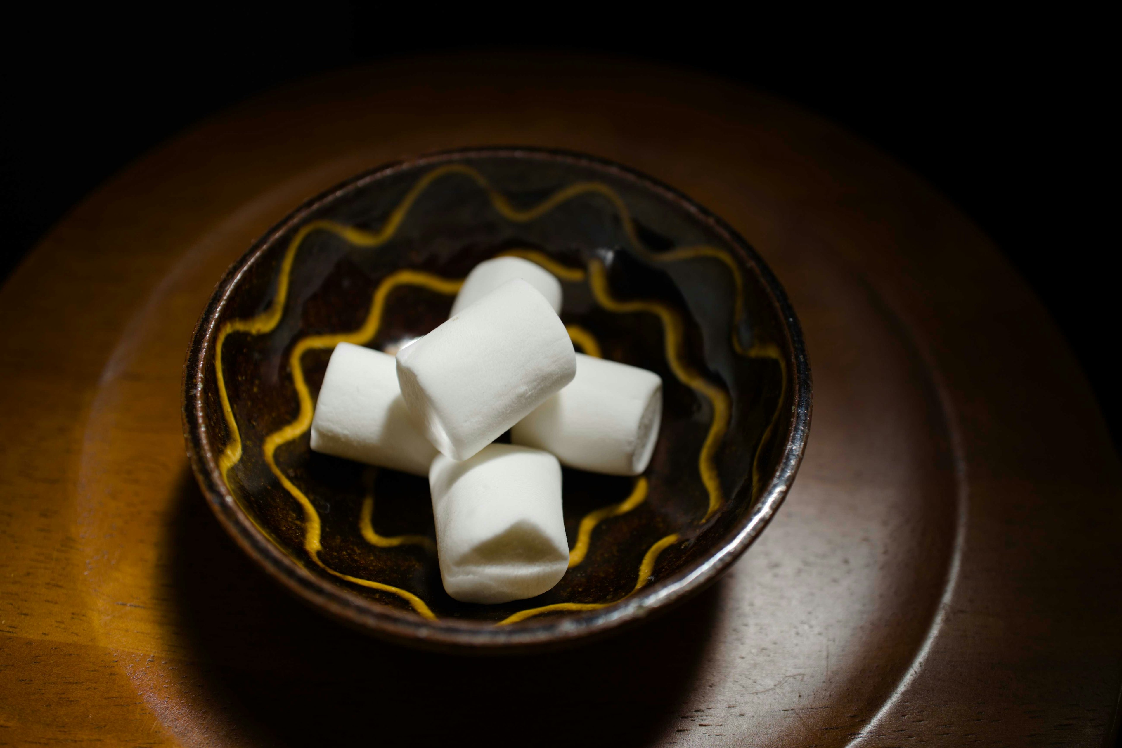 A brown bowl with white marshmallows on a black background