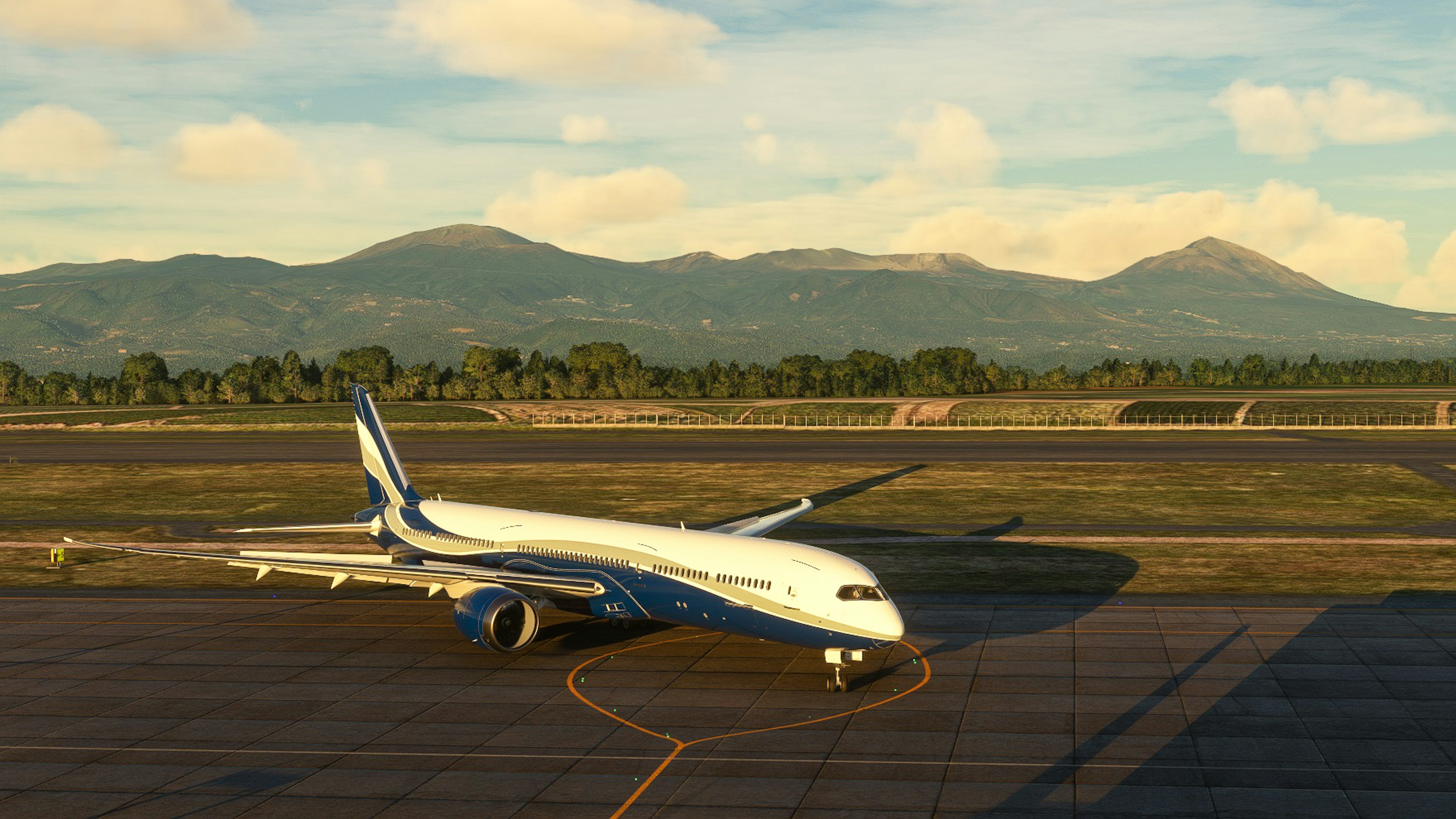 A blue and white aircraft parked on the runway with mountains in the background