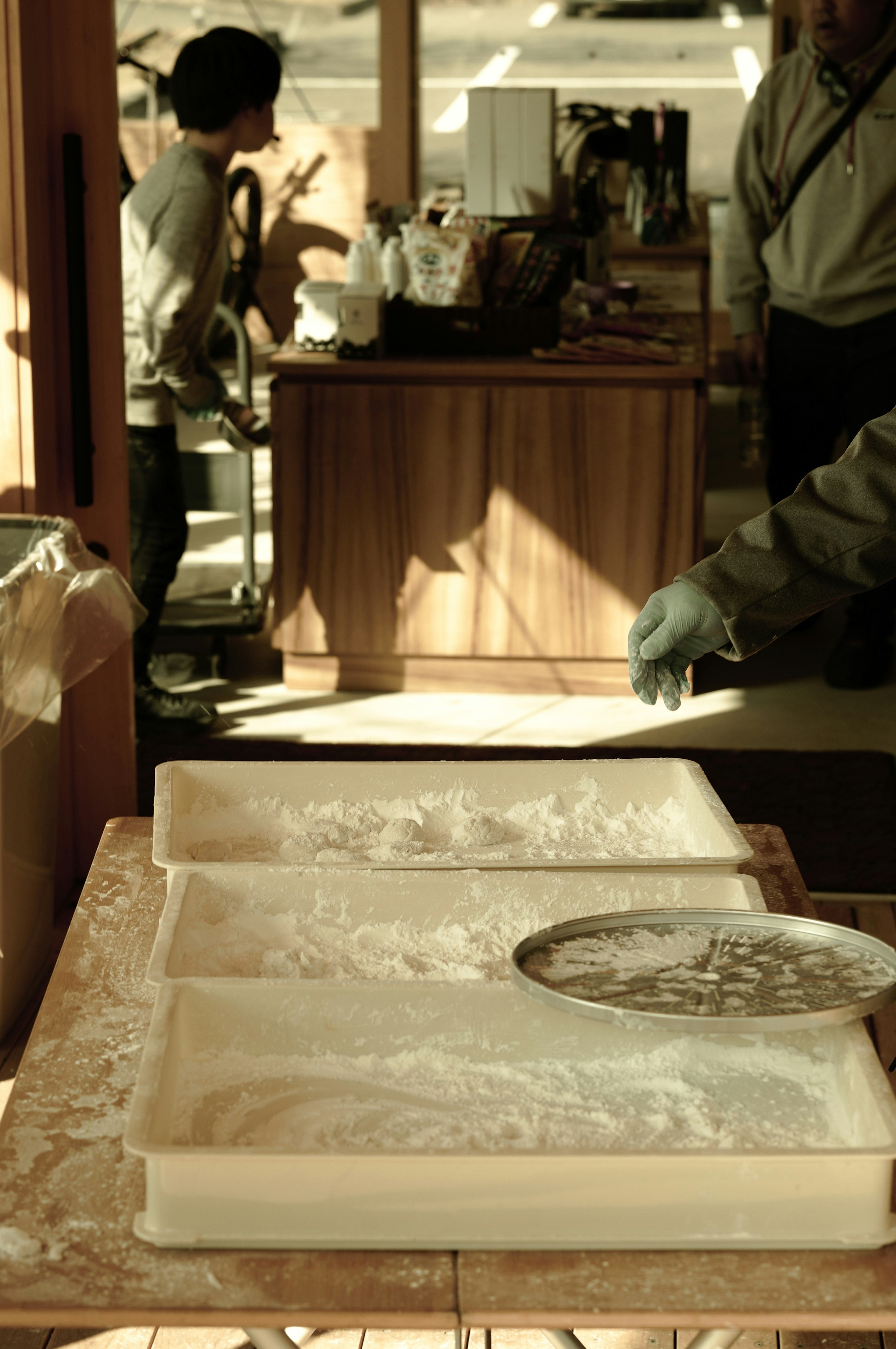 A workspace with trays of flour in the foreground and a person standing in the background