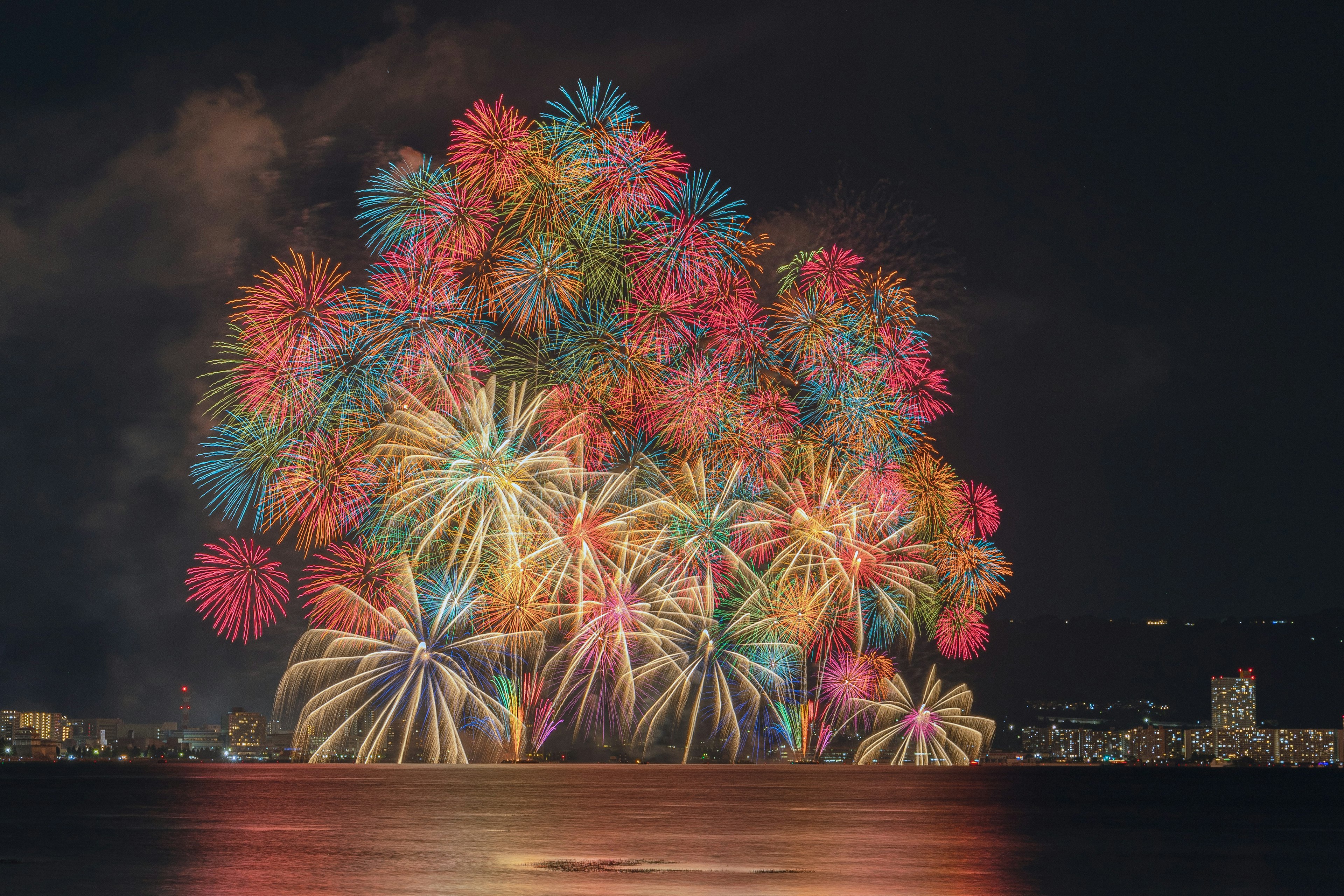 夜空に打ち上げられた色とりどりの花火が水面に映る美しい光景