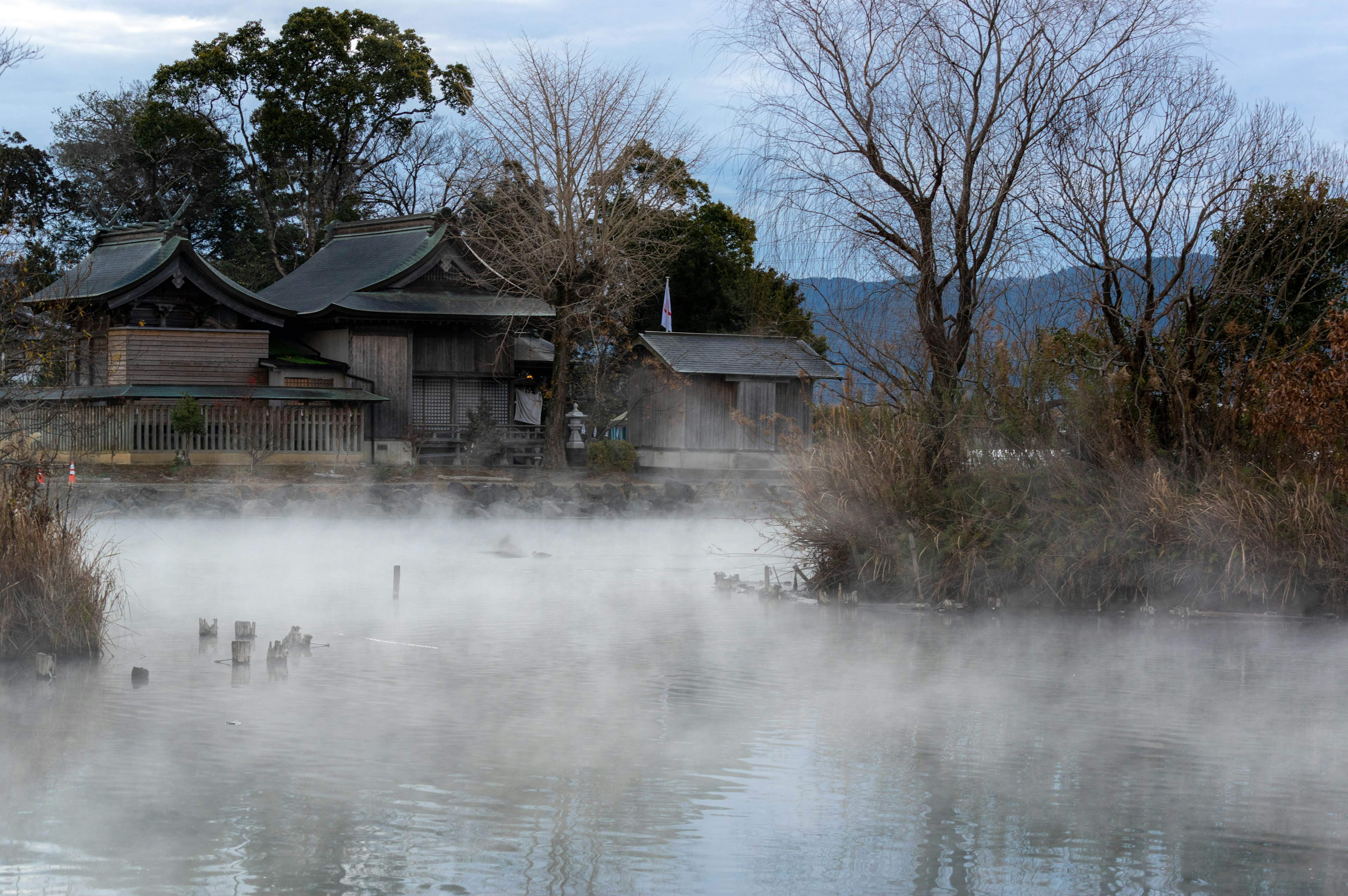 Paysage brumeux avec un étang et des bâtiments traditionnels