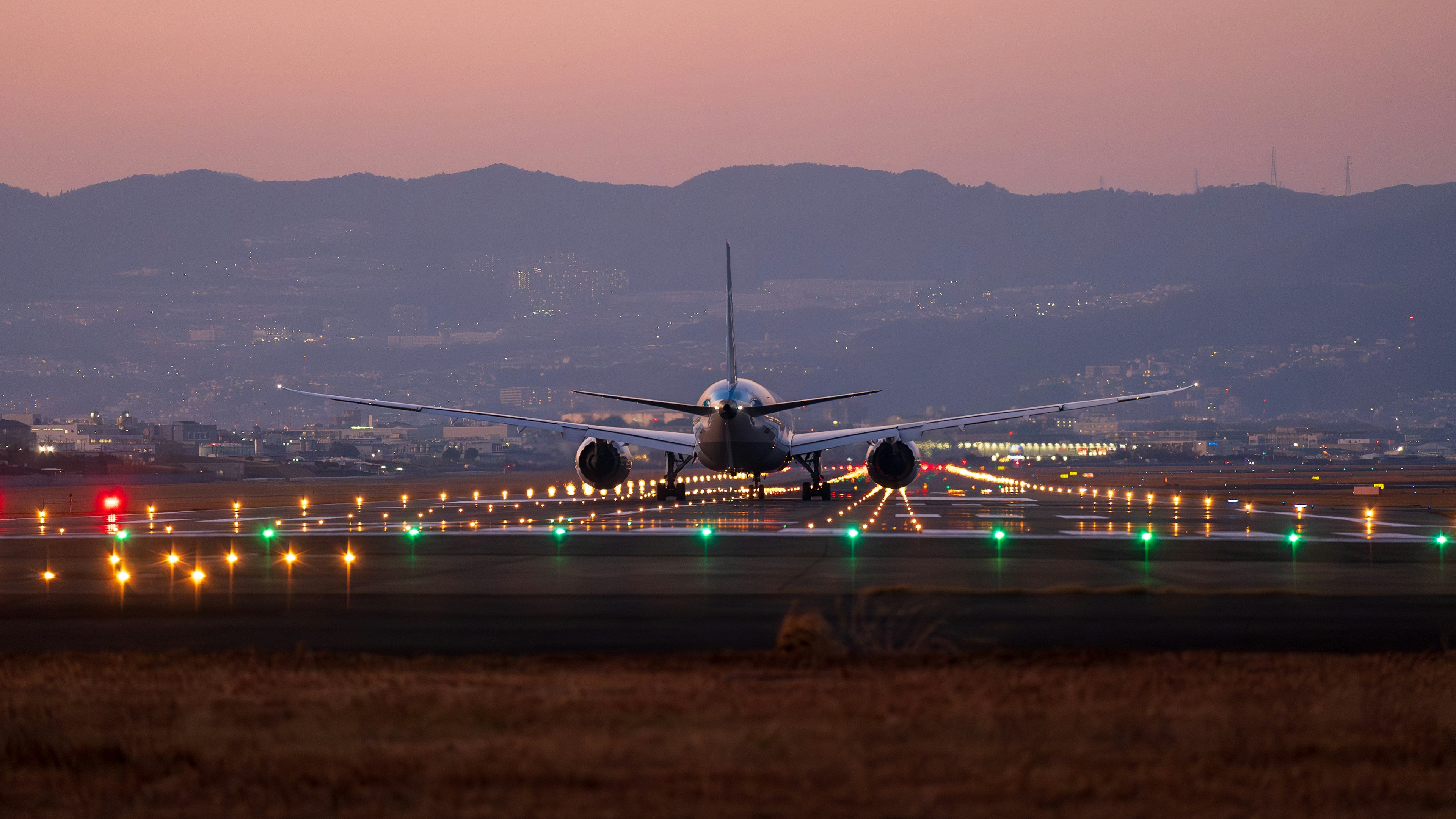 Flugzeug auf der Startbahn bei Dämmerung mit umliegenden Lichtern