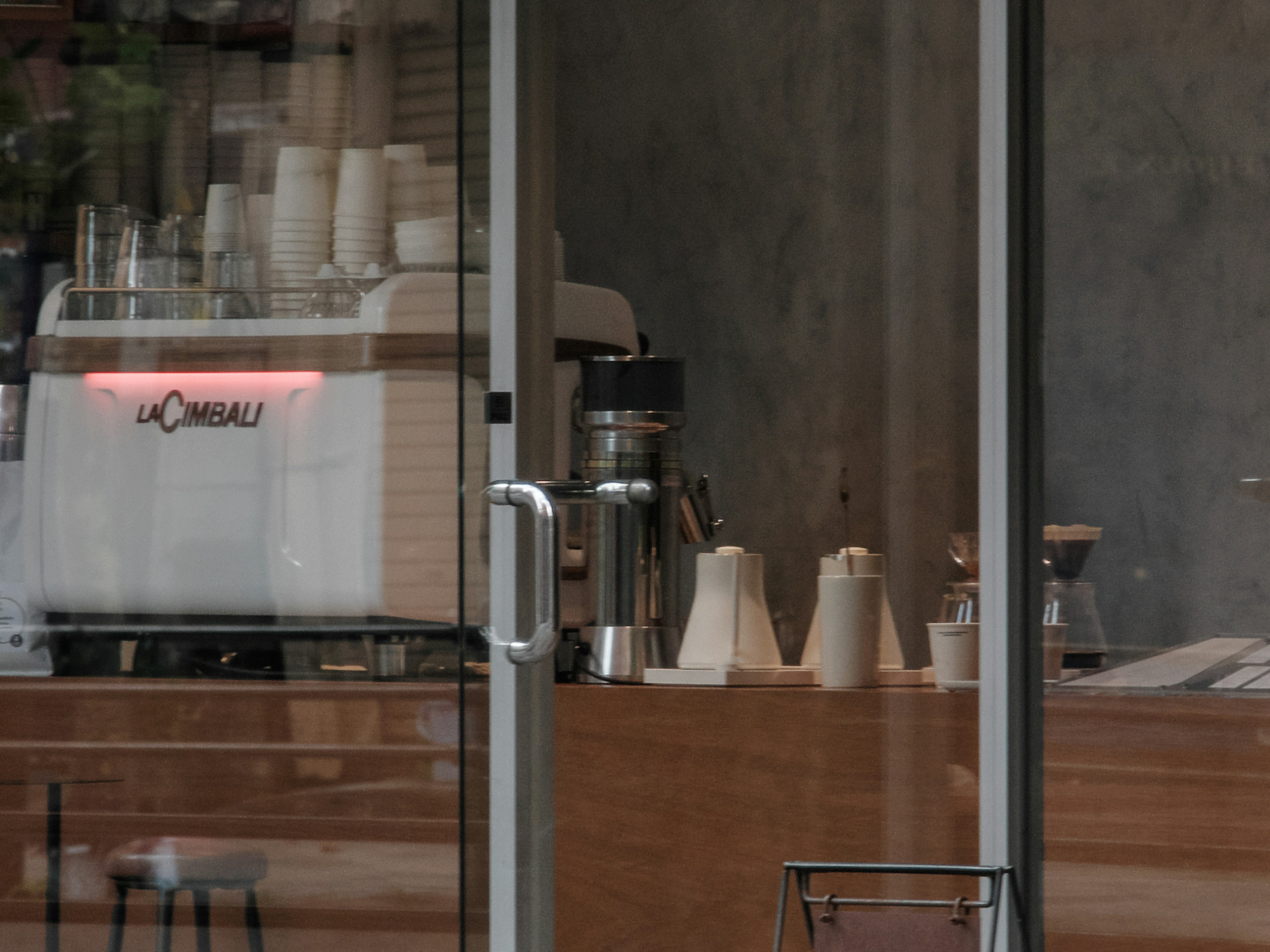 Interior de una cafetería visible a través de puertas de vidrio con una máquina de espresso elegante y equipo de café