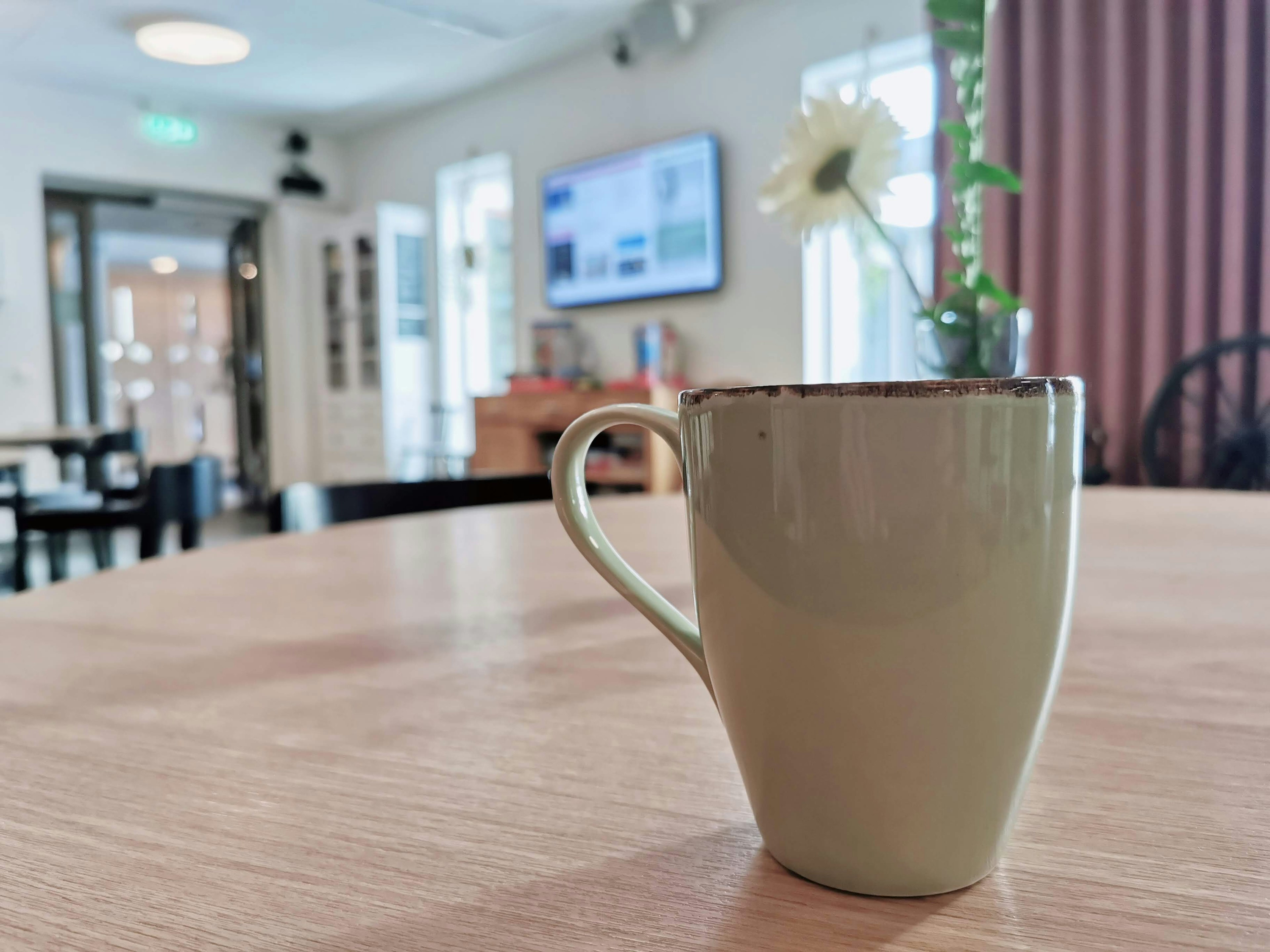 Una taza de café verde sobre una mesa con una flor al fondo