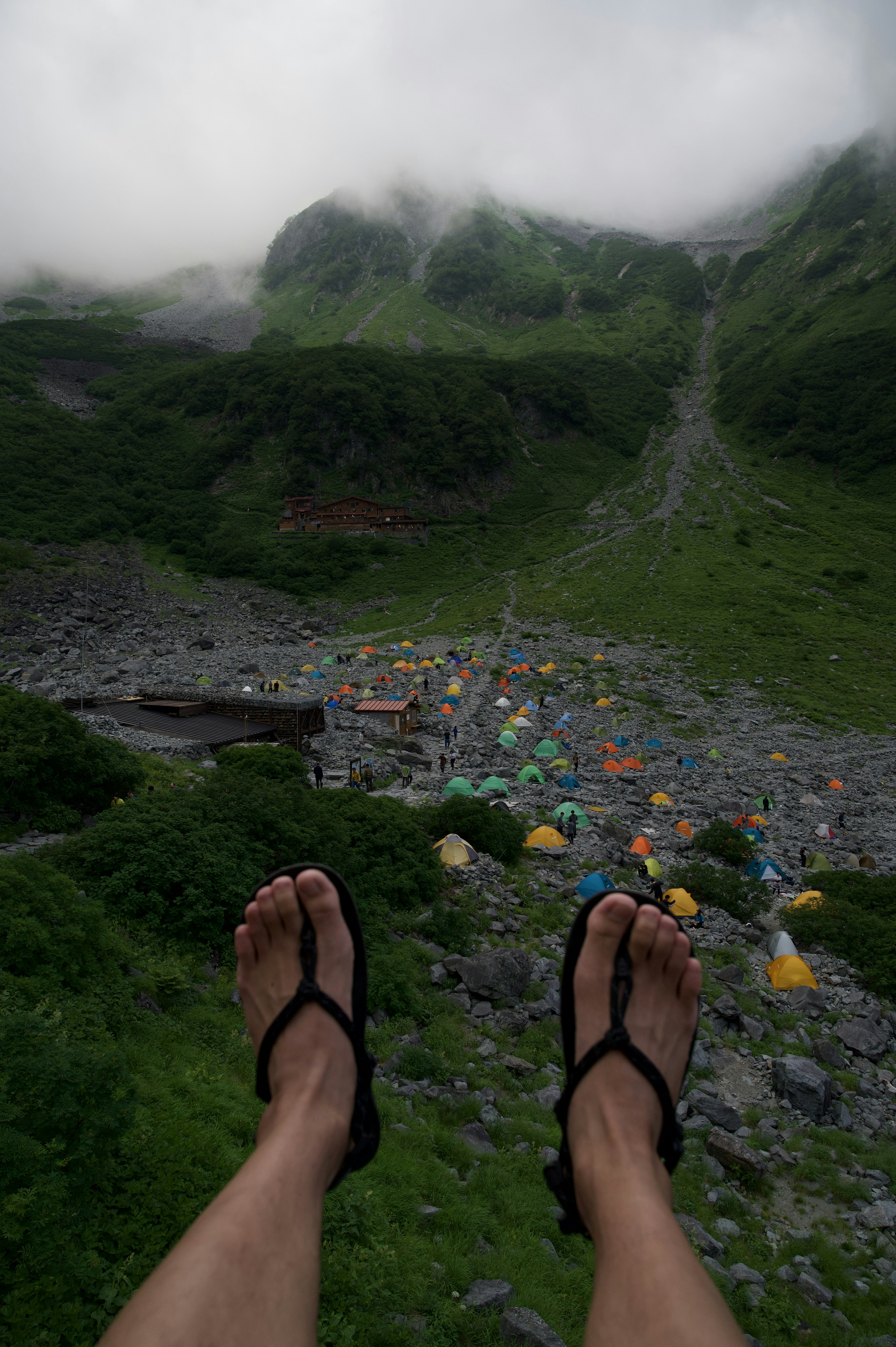 Feet in sandals overlooking a foggy mountain landscape and a colorful campsite