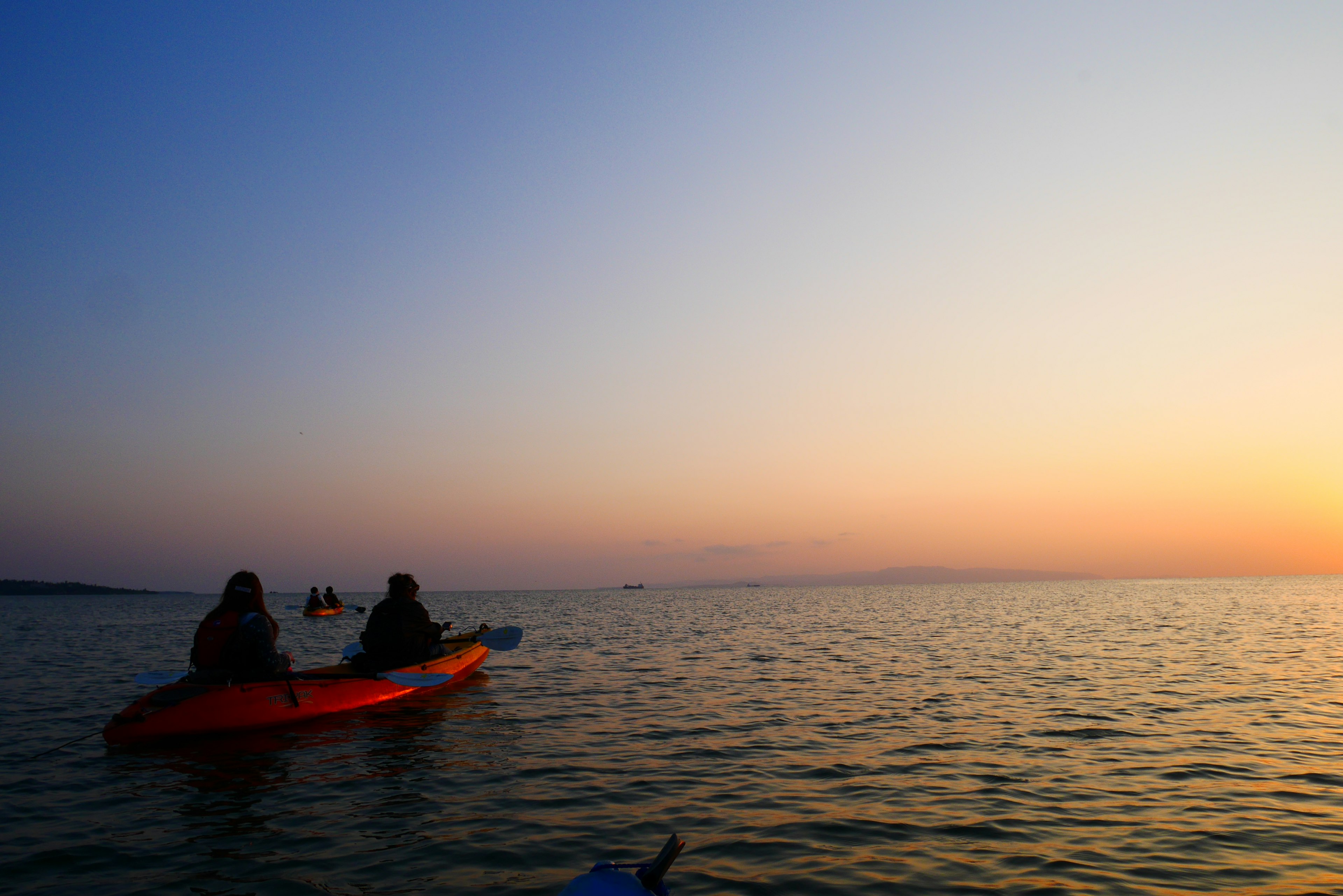 夕暮れの海でカヤックを漕ぐ人々のシルエット