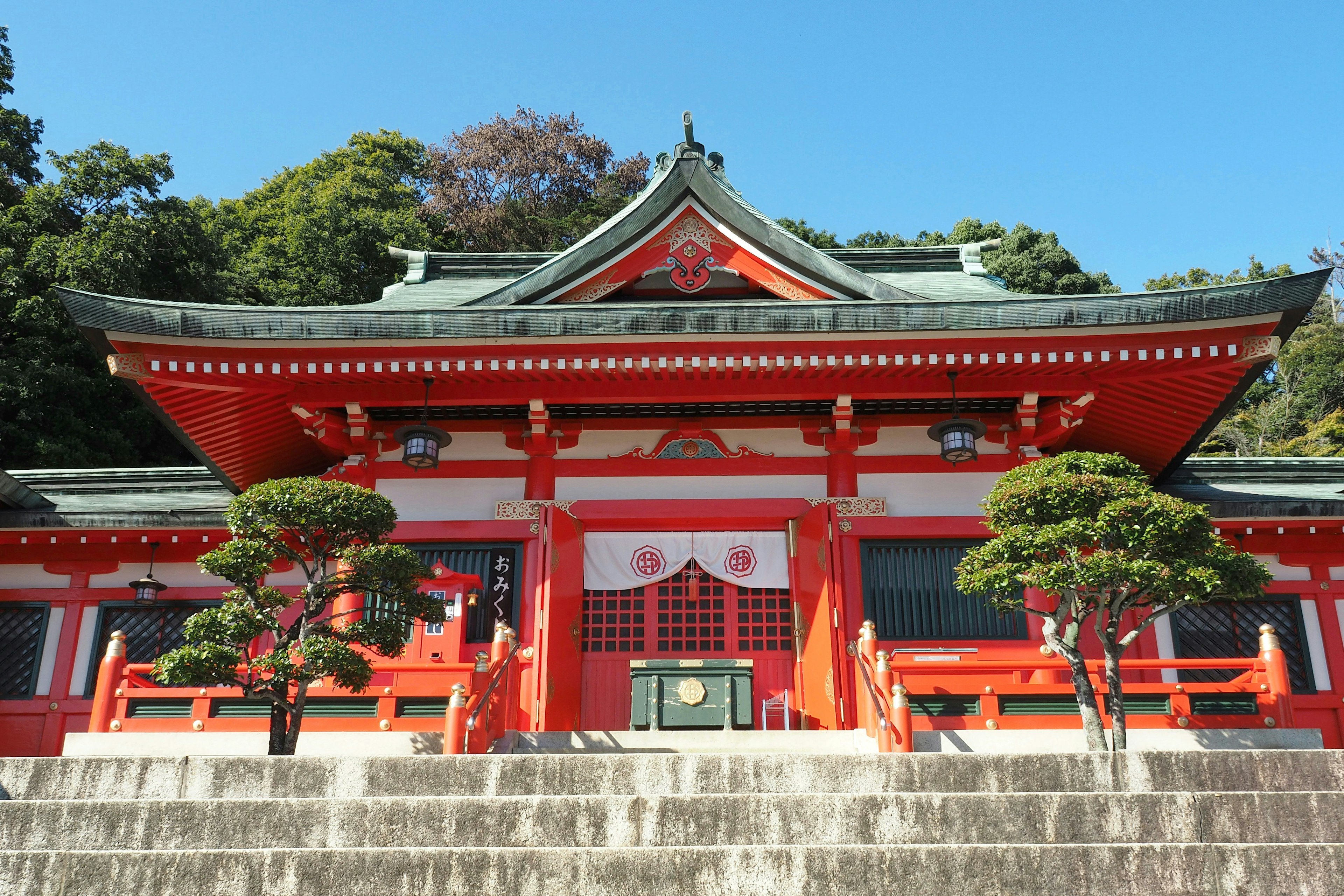 A beautiful shrine with a red roof stands under a blue sky