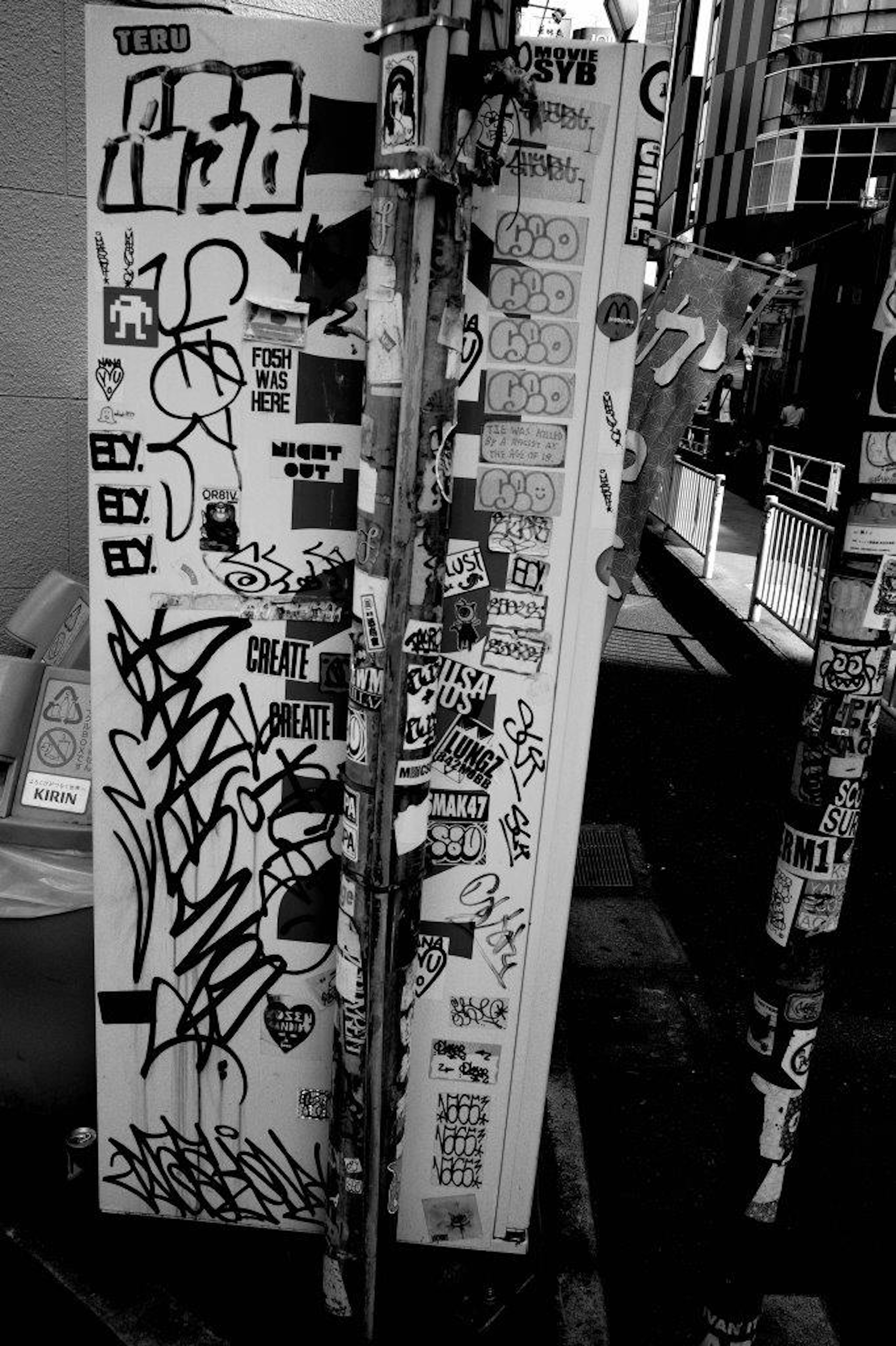 Image en noir et blanc d'un poteau de rue couvert de stickers et de graffitis