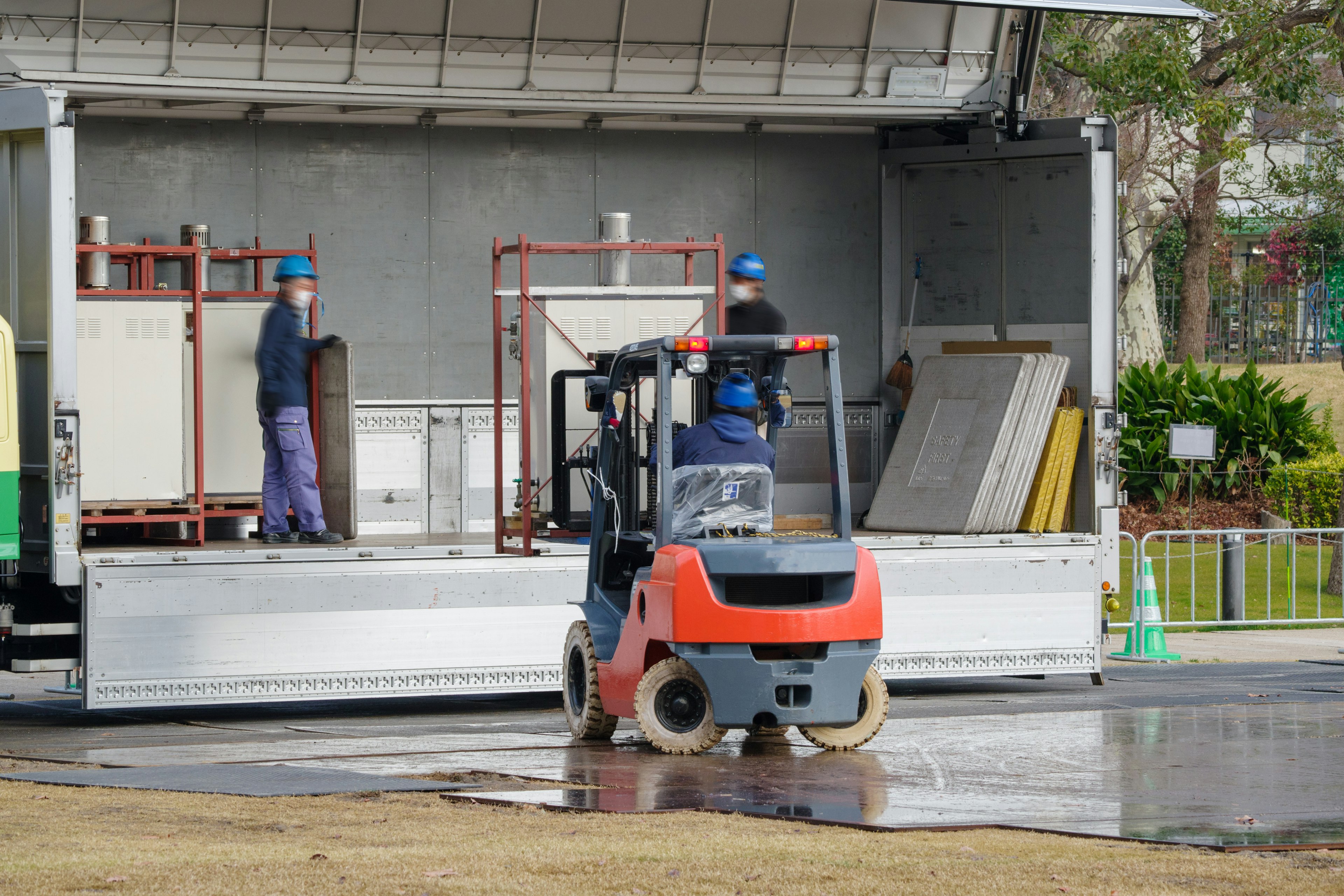 フォークリフトで荷物を運ぶ作業員二人の画像