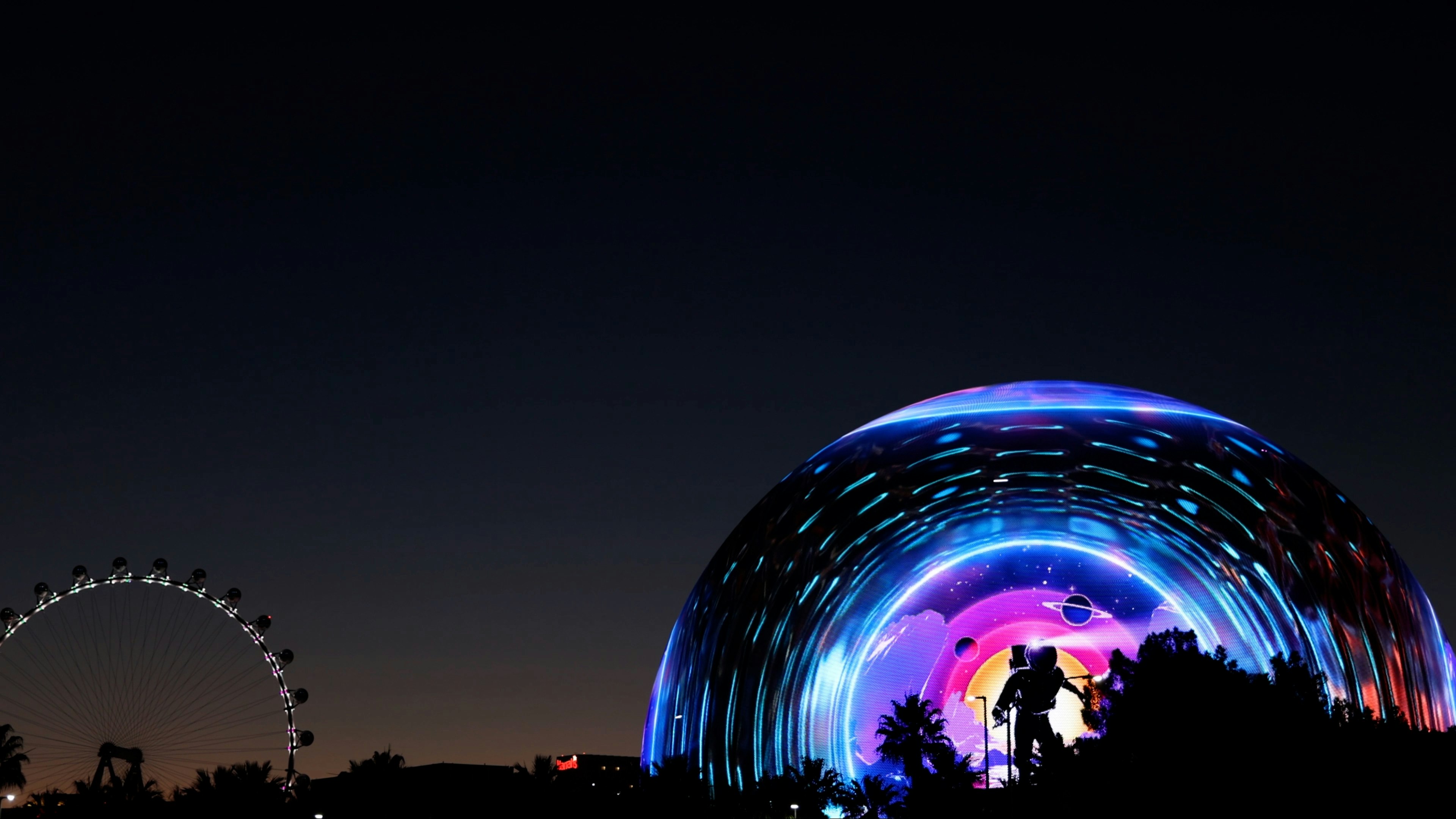 Colorful dome illuminated at night with a silhouette of a Ferris wheel