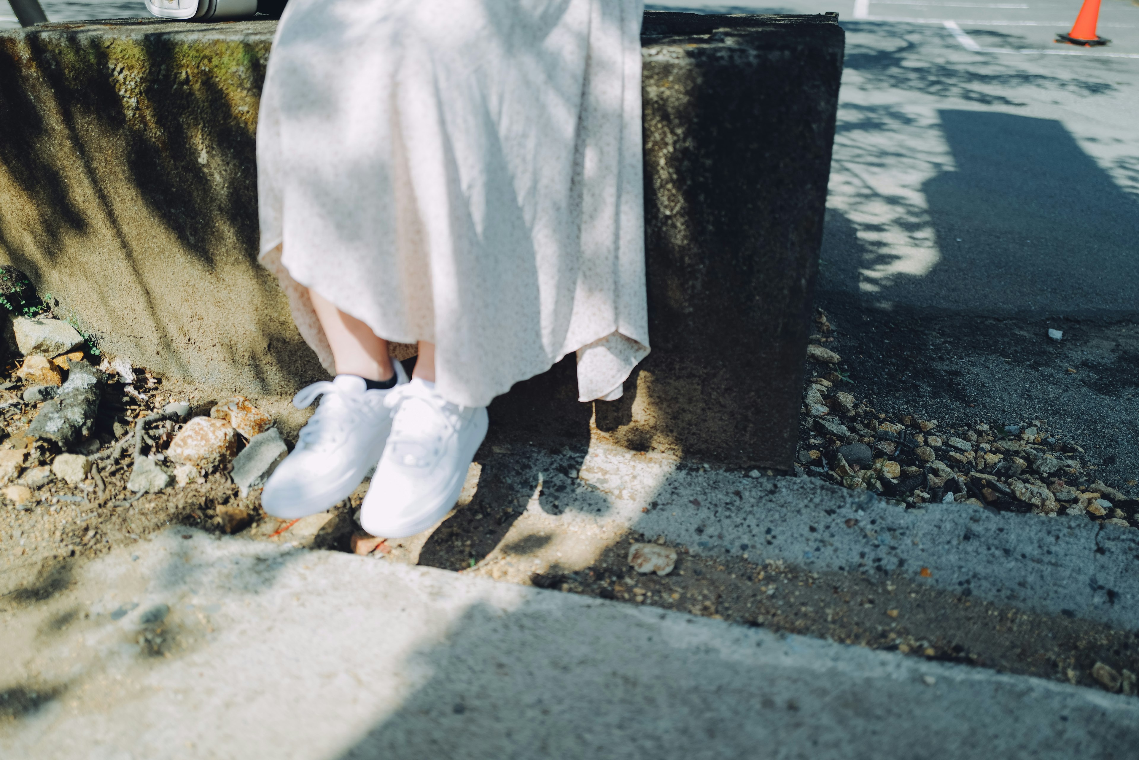 Die Füße einer Frau in weißen Sneakers, die auf einer Betonkante sitzen, während sie ein weißes Kleid trägt