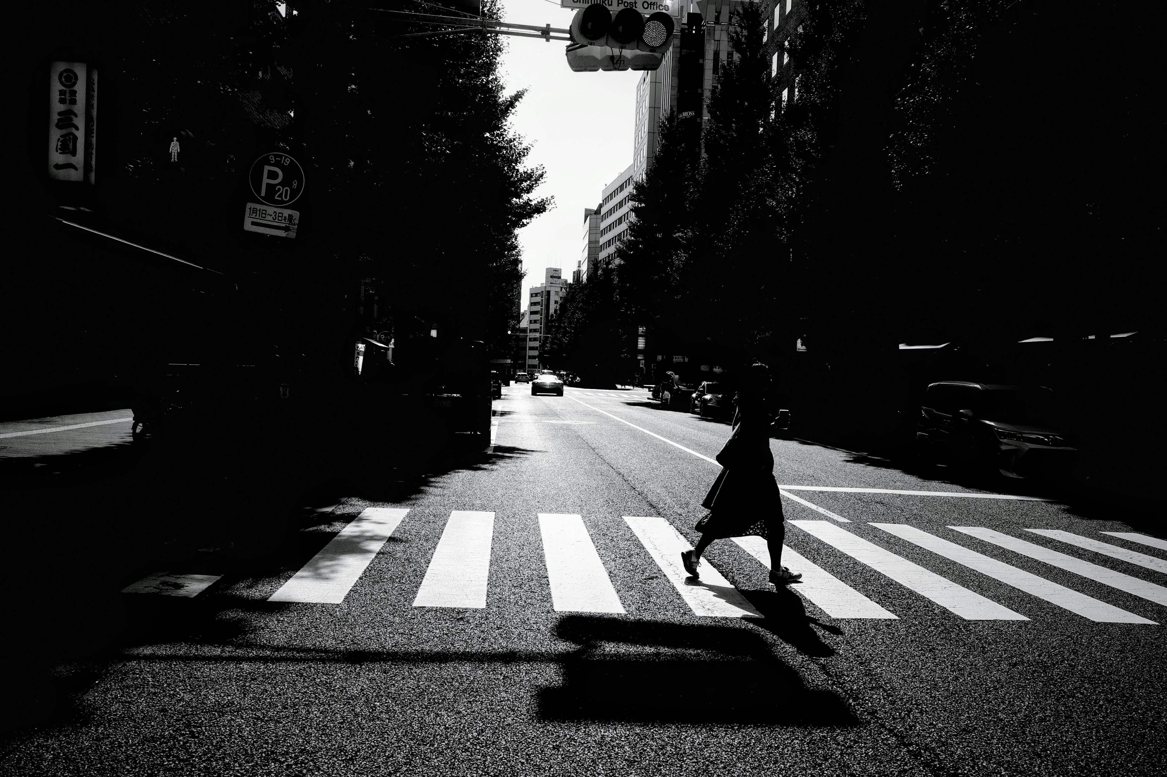 Silhouette d'une personne traversant un passage piéton rayé noir et blanc dans une rue de la ville