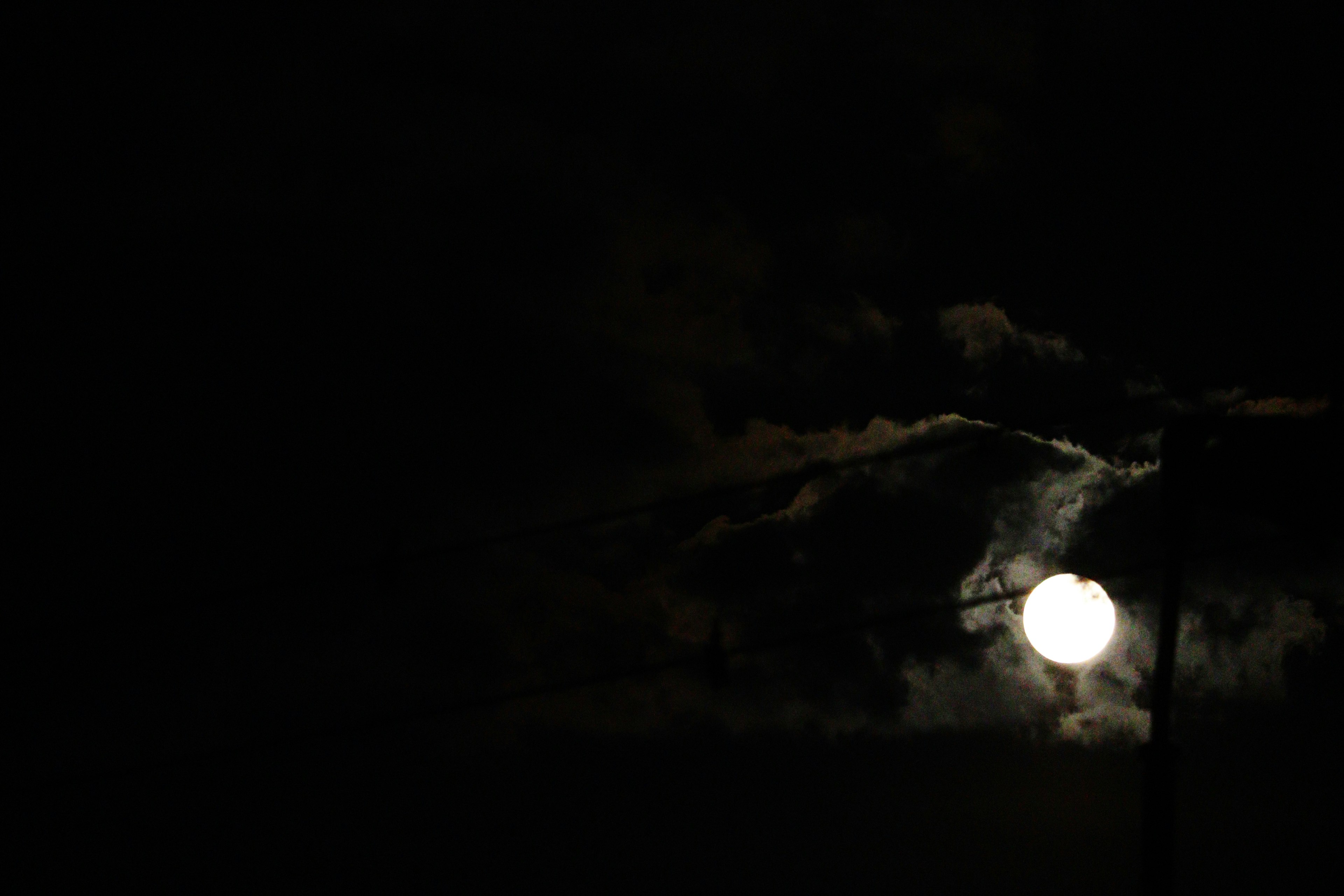 Luna llena brillante en un cielo oscuro con siluetas de nubes