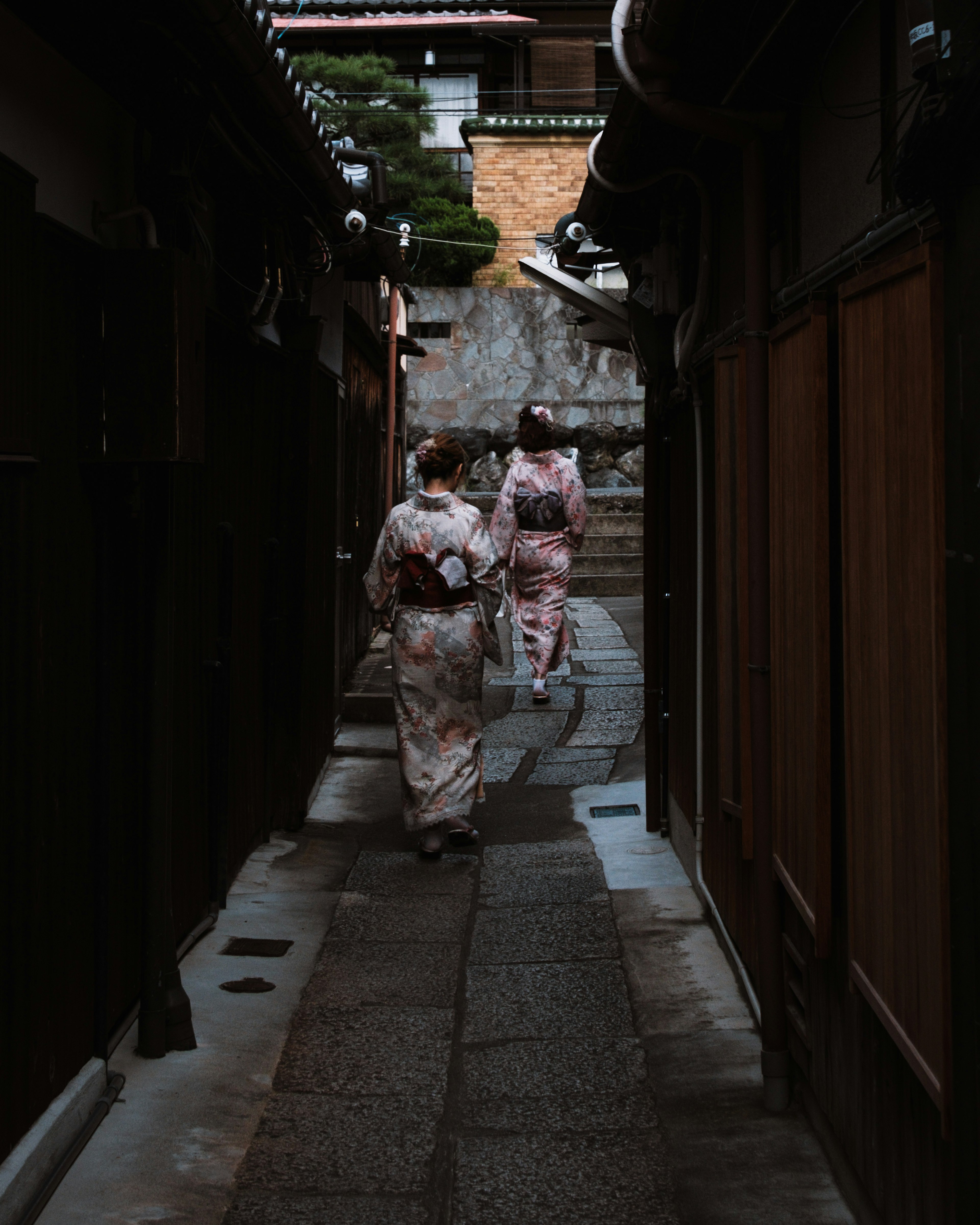 Two women in kimonos walking down a narrow alley