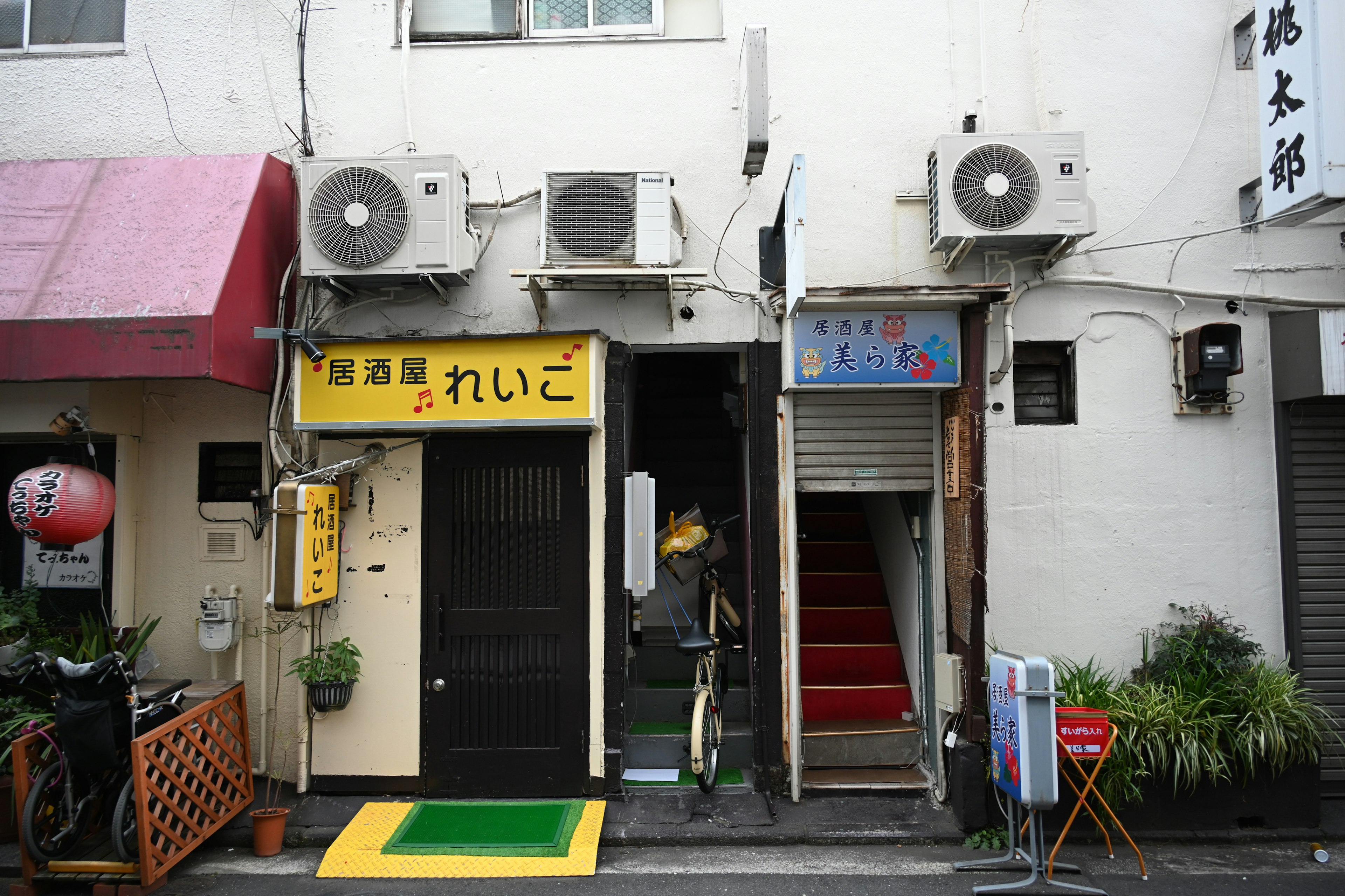 Una escena callejera con la entrada de un restaurante con un letrero amarillo y escaleras rojas