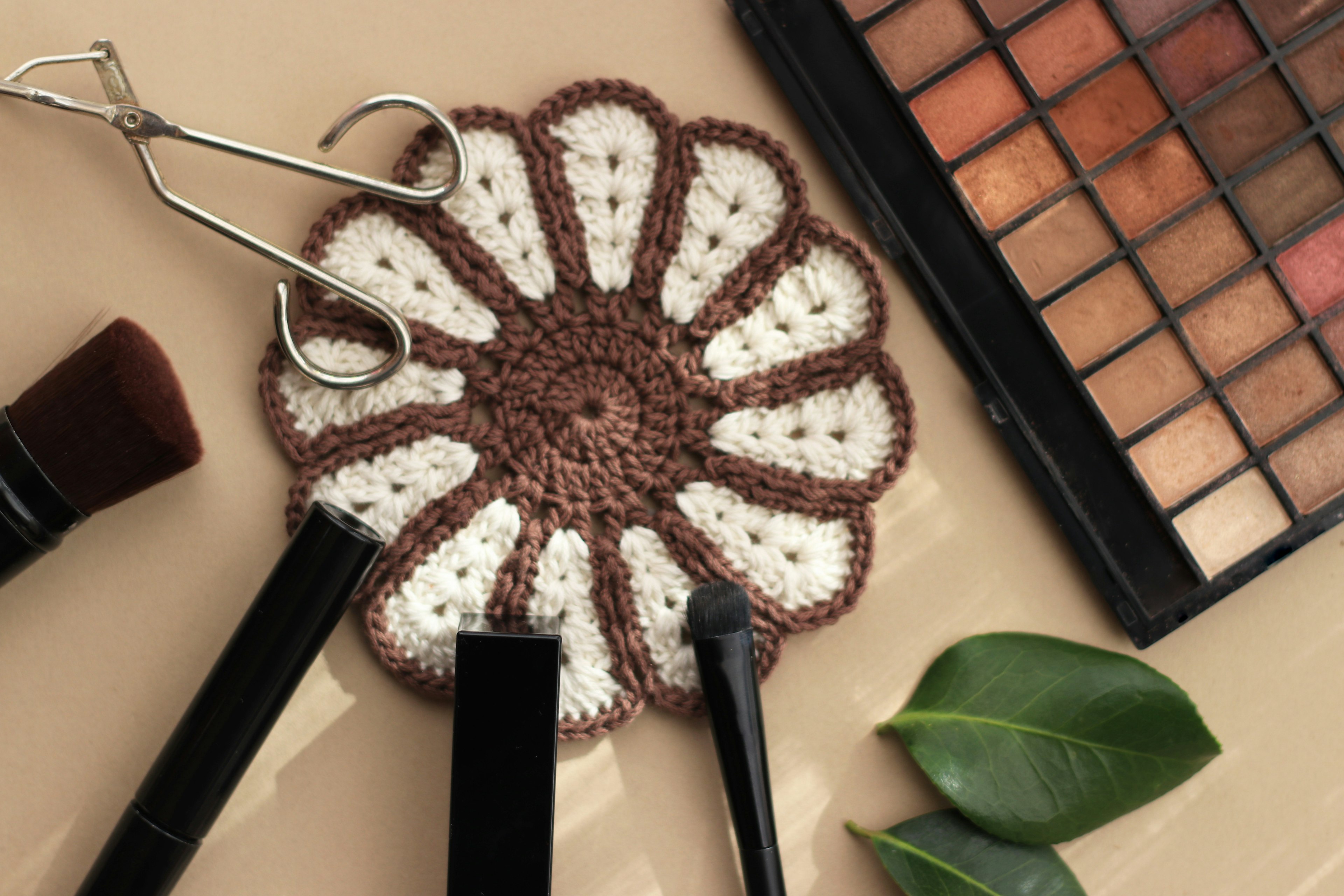 A flower-shaped crochet coaster with makeup brushes and an eyeshadow palette placed on it