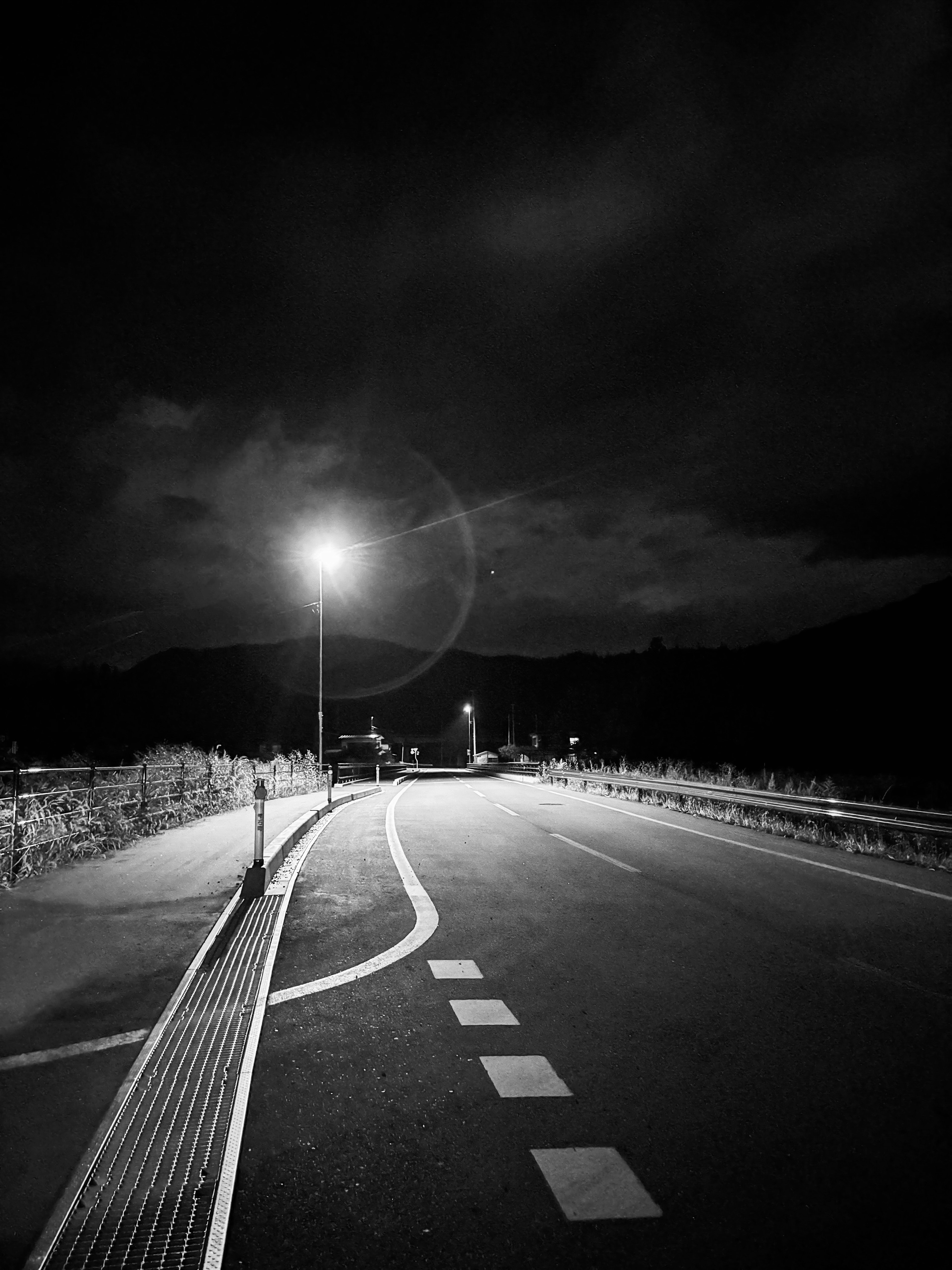 Black and white photograph of a winding road illuminated by a streetlight at night