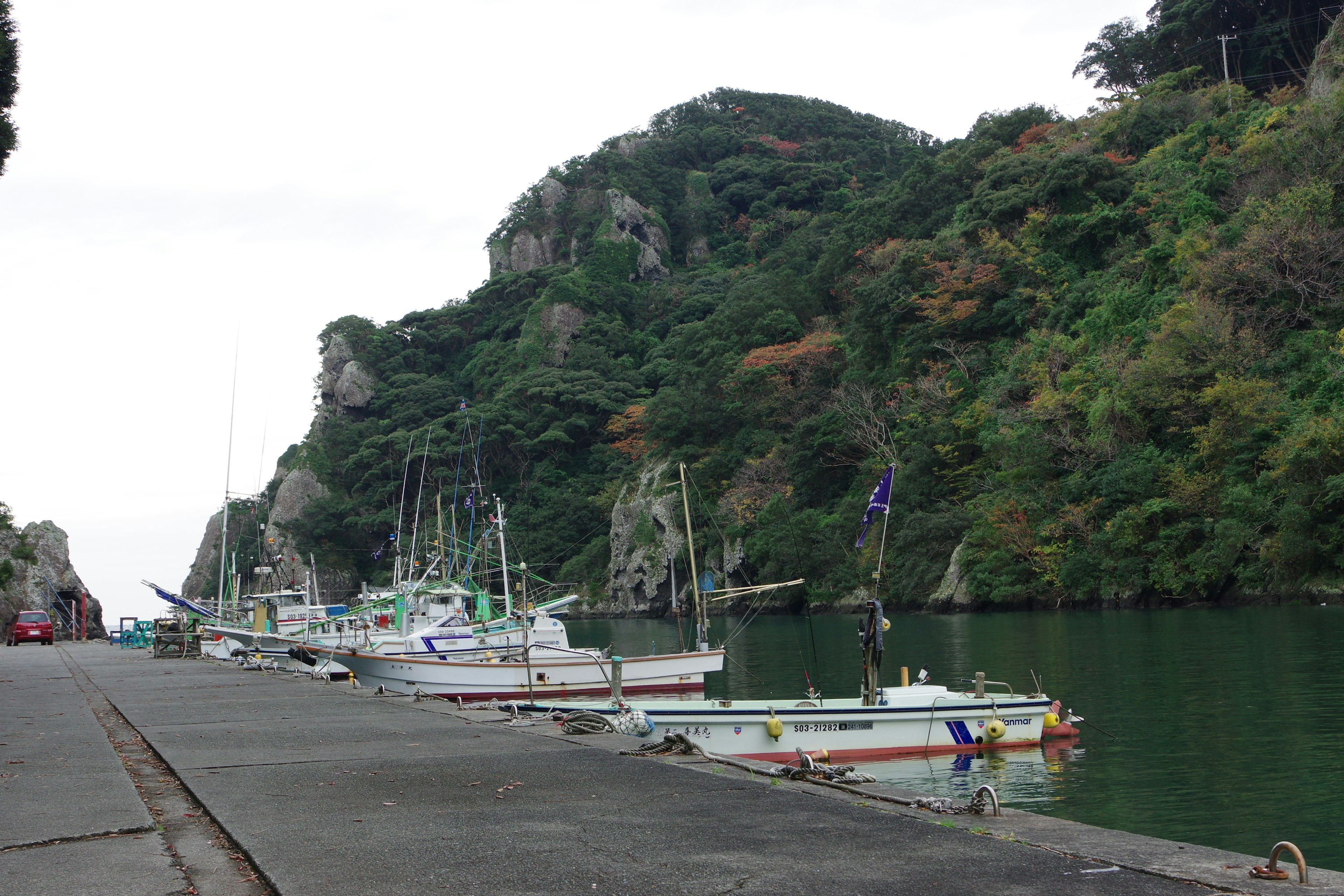 Fishing boats docked at a quiet harbor with lush green hills