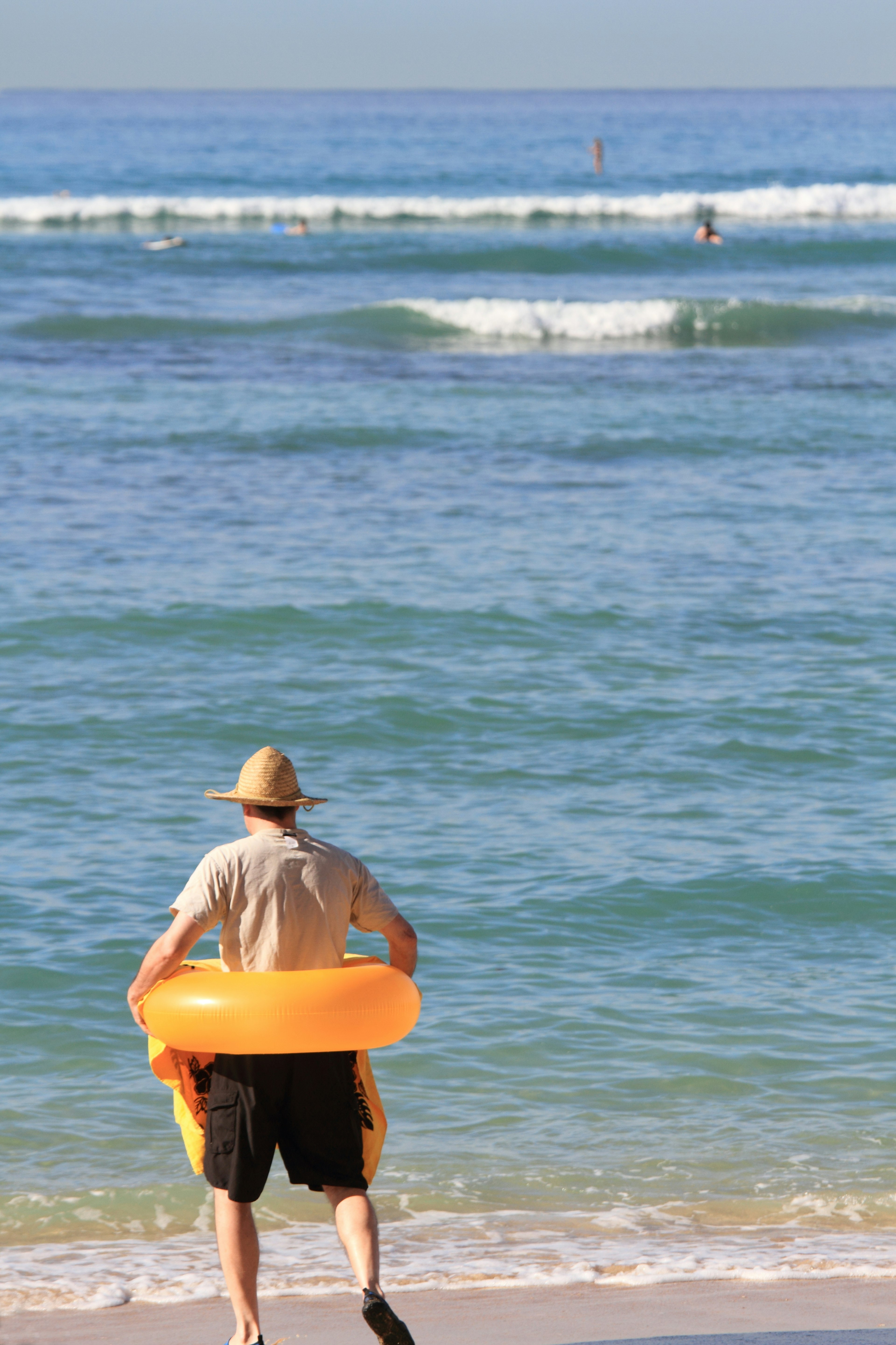 海に向かう人がオレンジ色の浮き輪を持っている