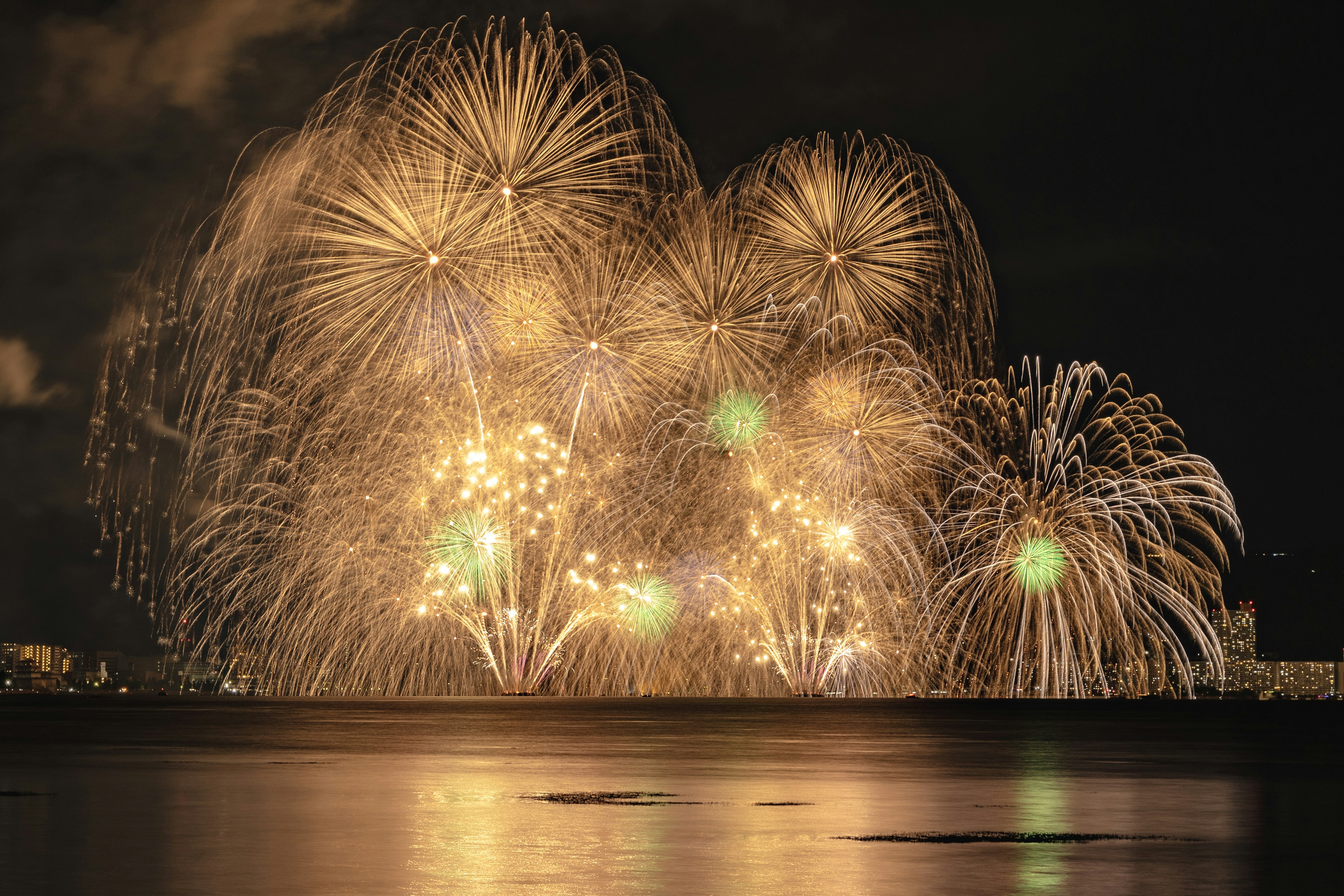 Spettacolari fuochi d'artificio dorati che illuminano il cielo notturno riflessi sull'acqua