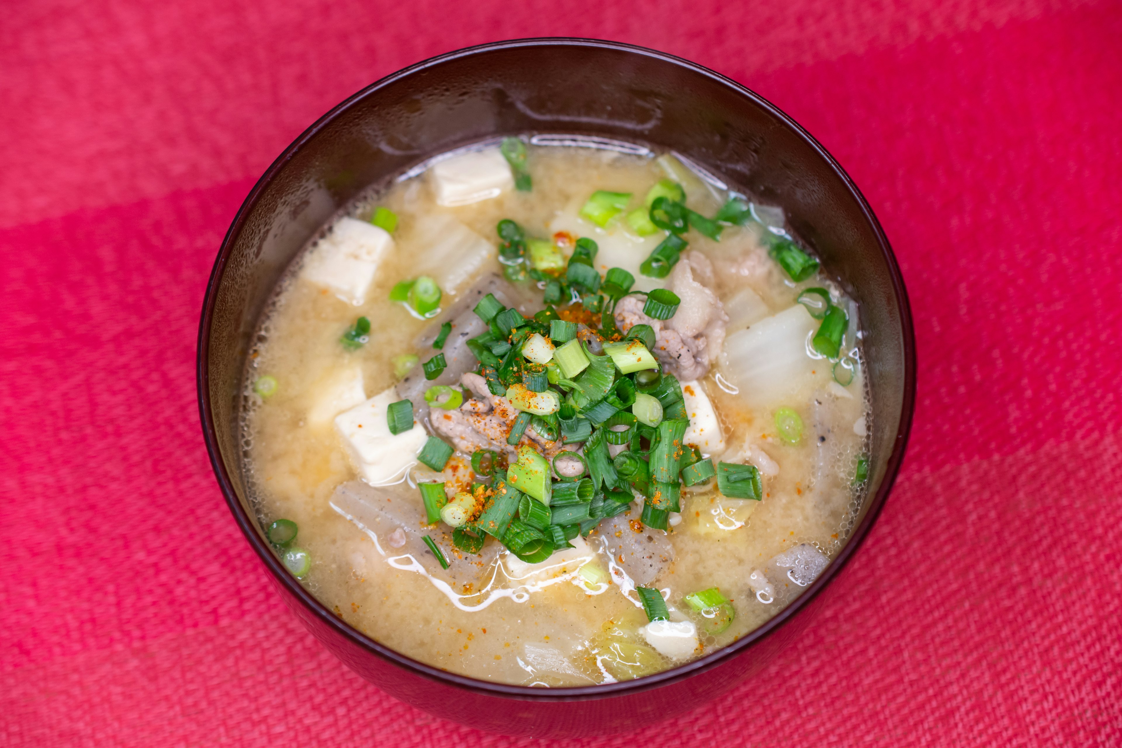 Mangkuk sup miso dengan tahu dan daun bawang di atas latar belakang merah