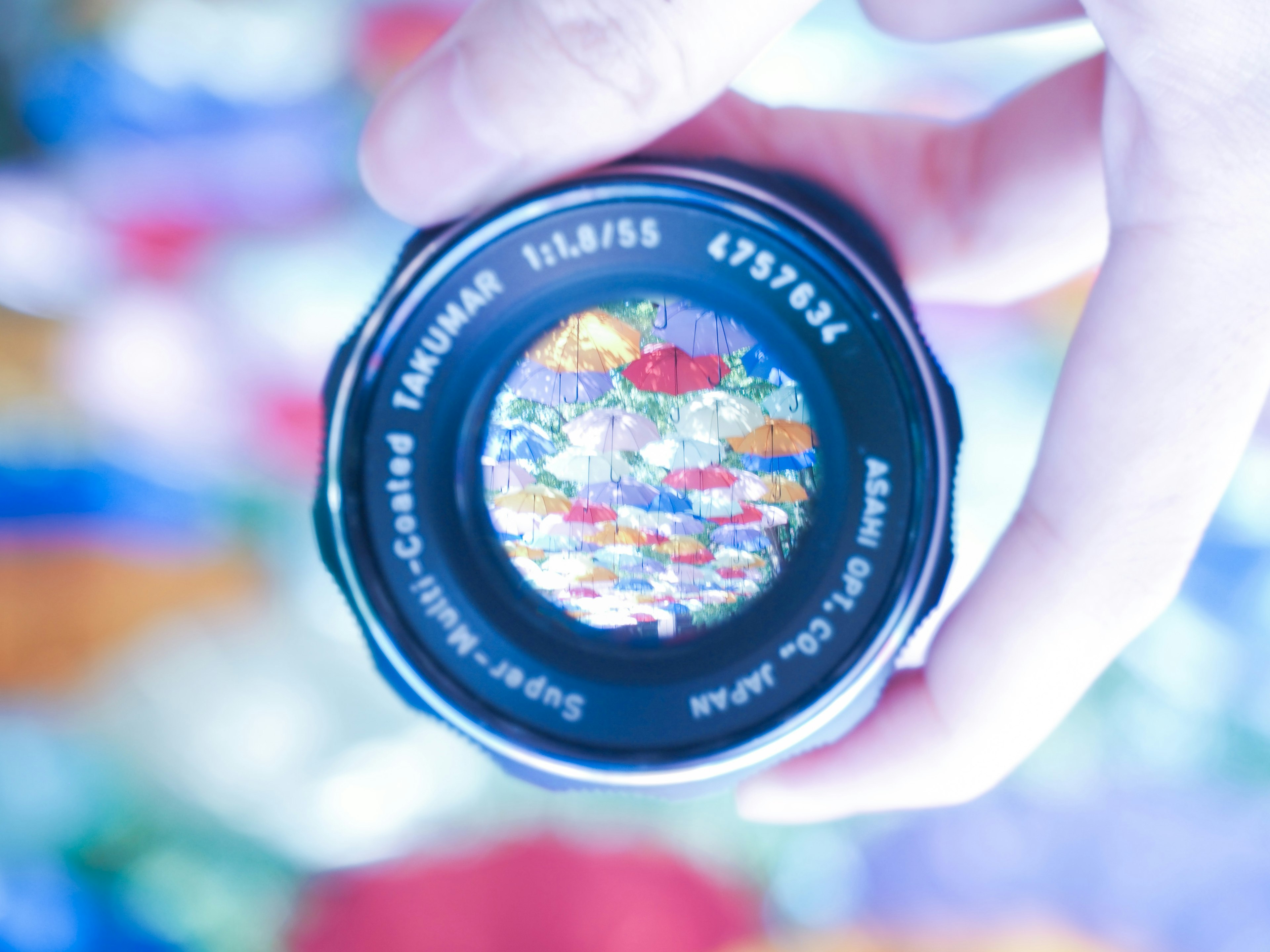 A hand holding a lens reflecting colorful umbrellas