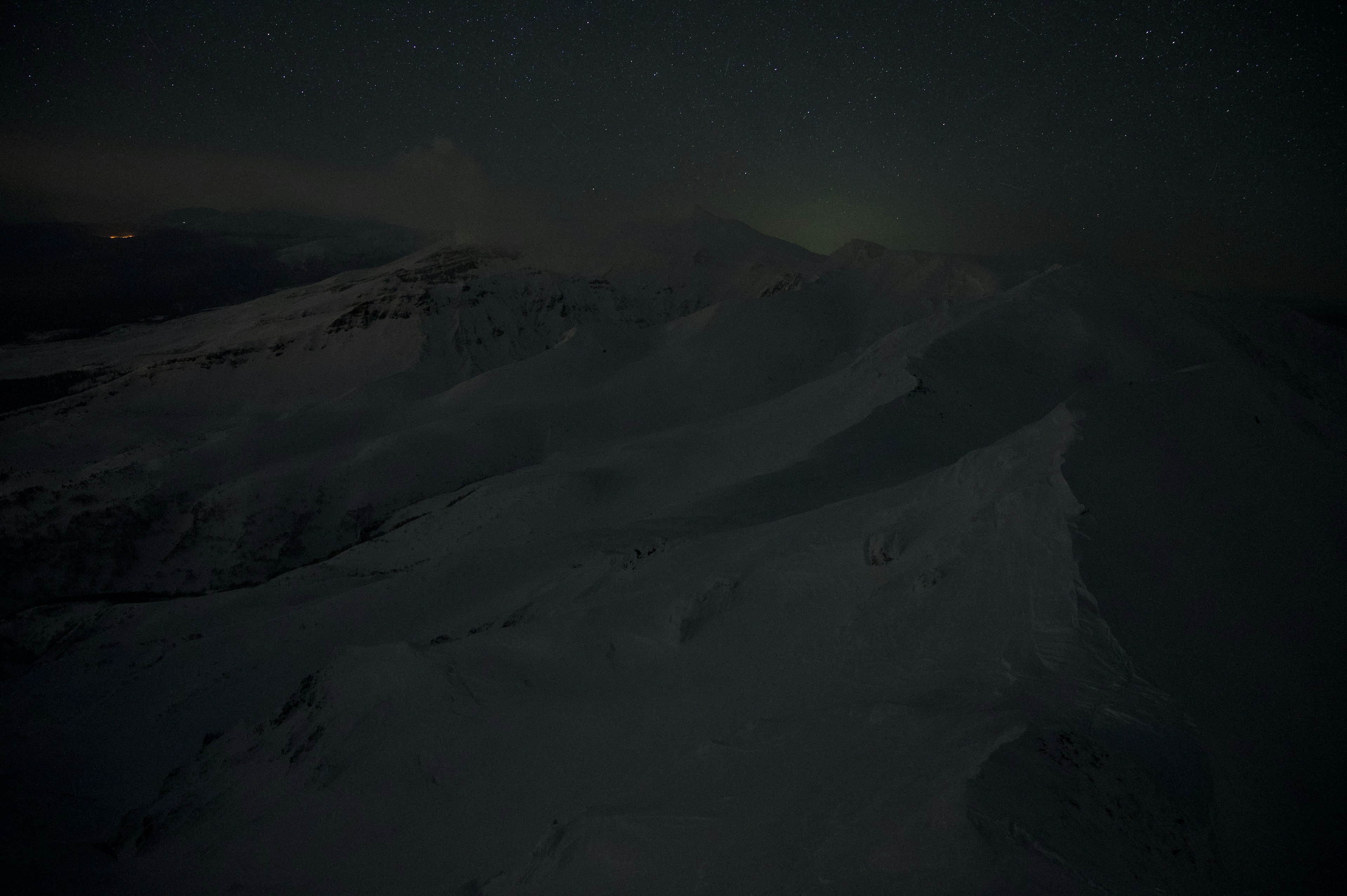 暗い夜空の下に広がる雪に覆われた山々の風景