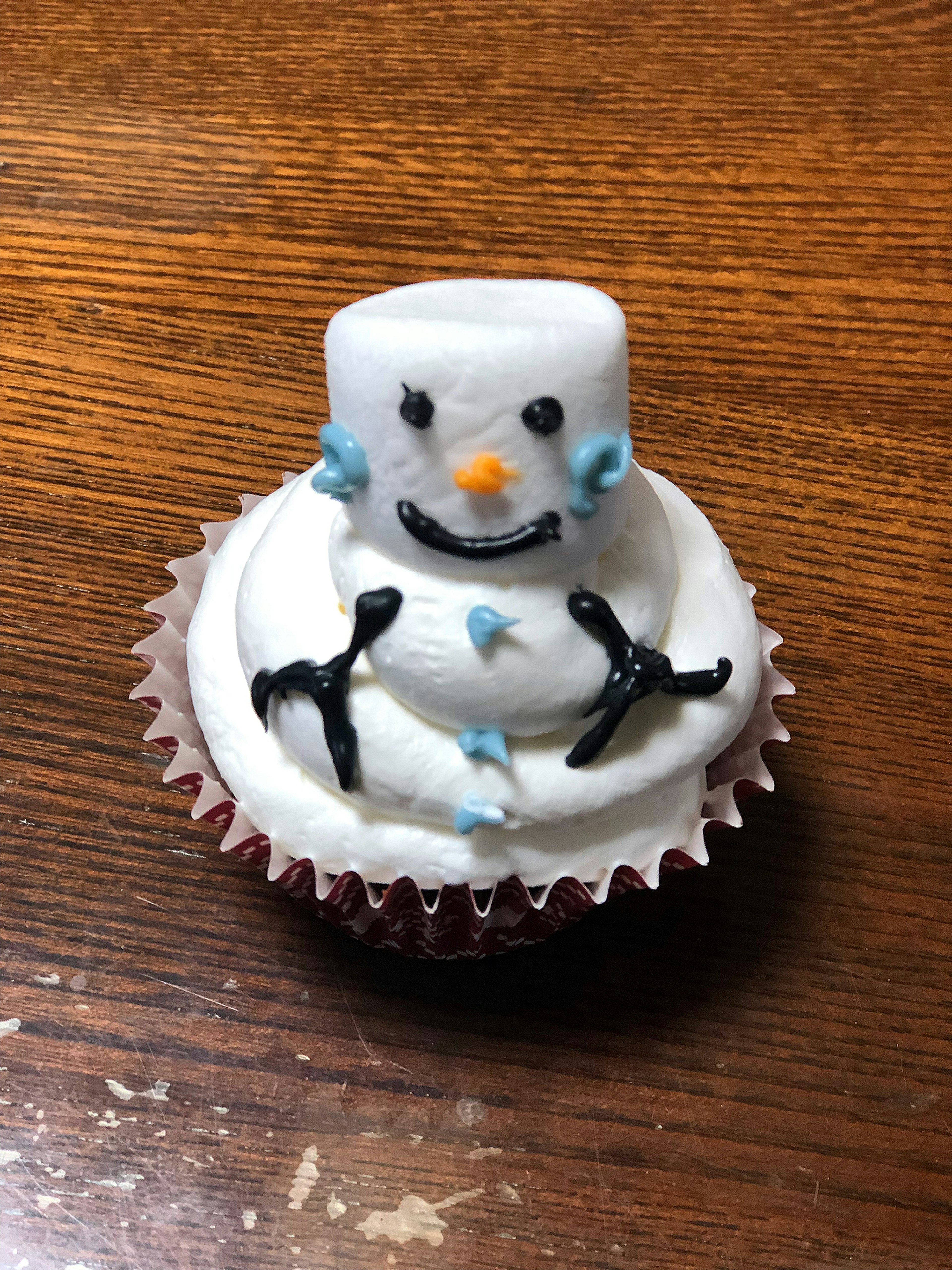 Cupcake designed as a snowman featuring white icing and a marshmallow head