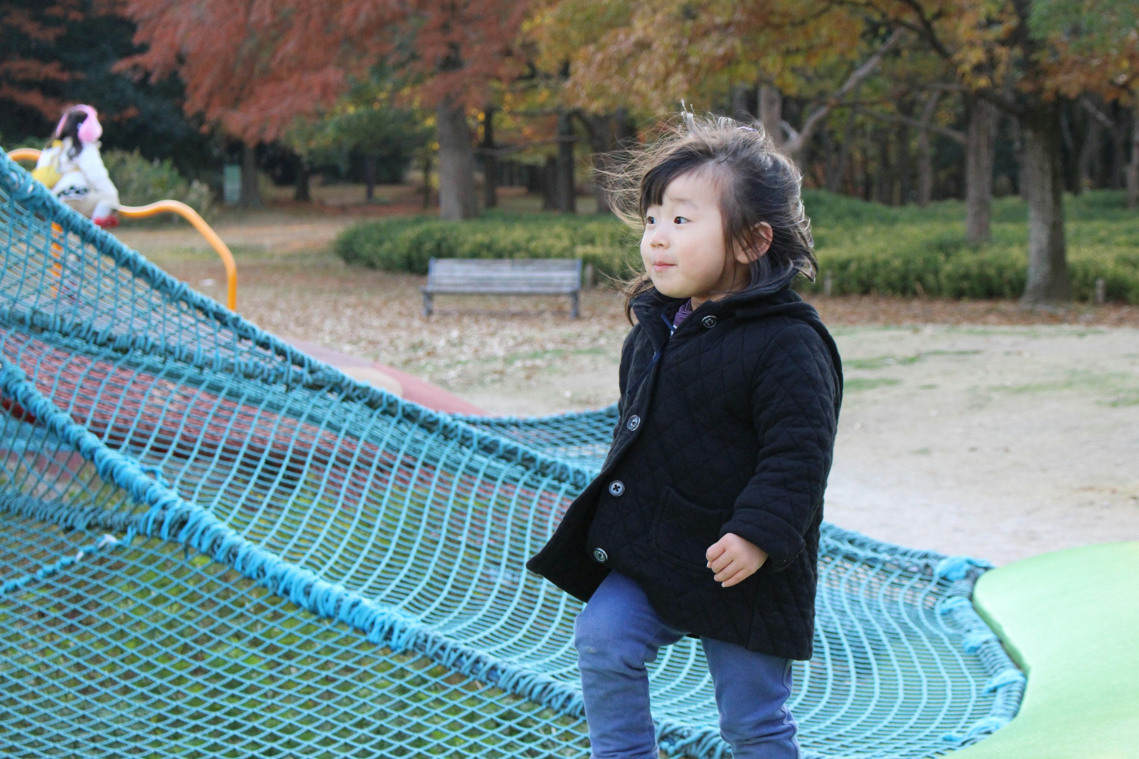 Child playing on a playground structure in a park smiling with autumn foliage in the background