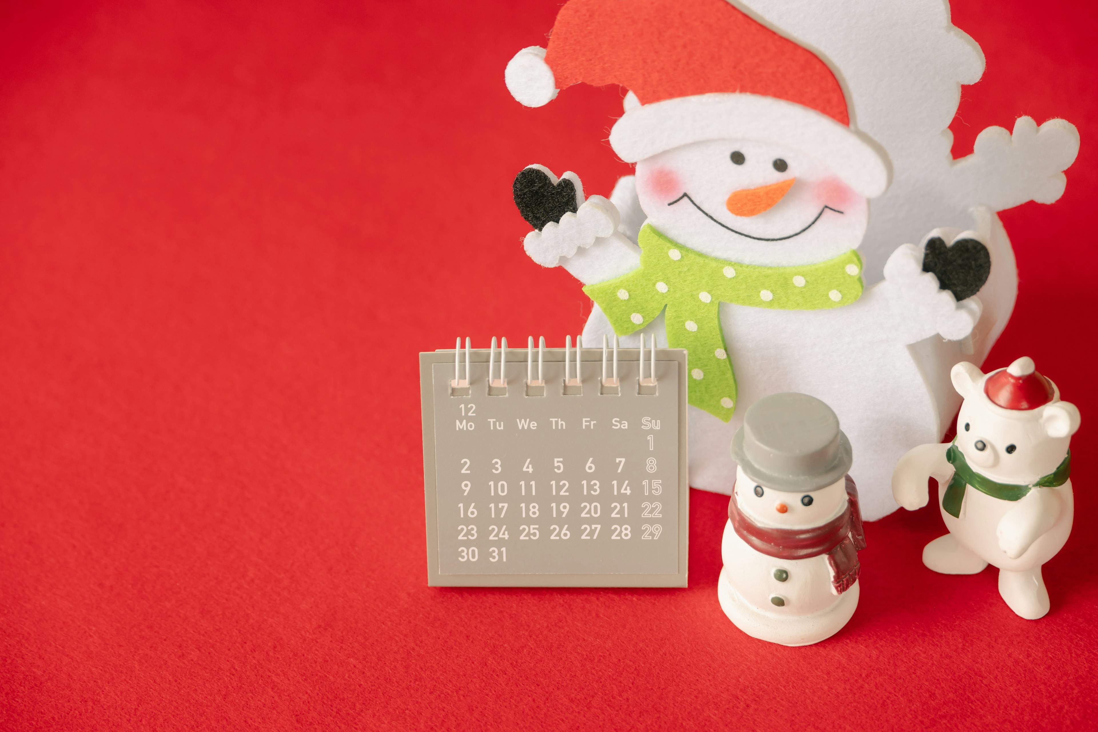 Muñeco de nieve con un calendario y decoraciones navideñas sobre fondo rojo