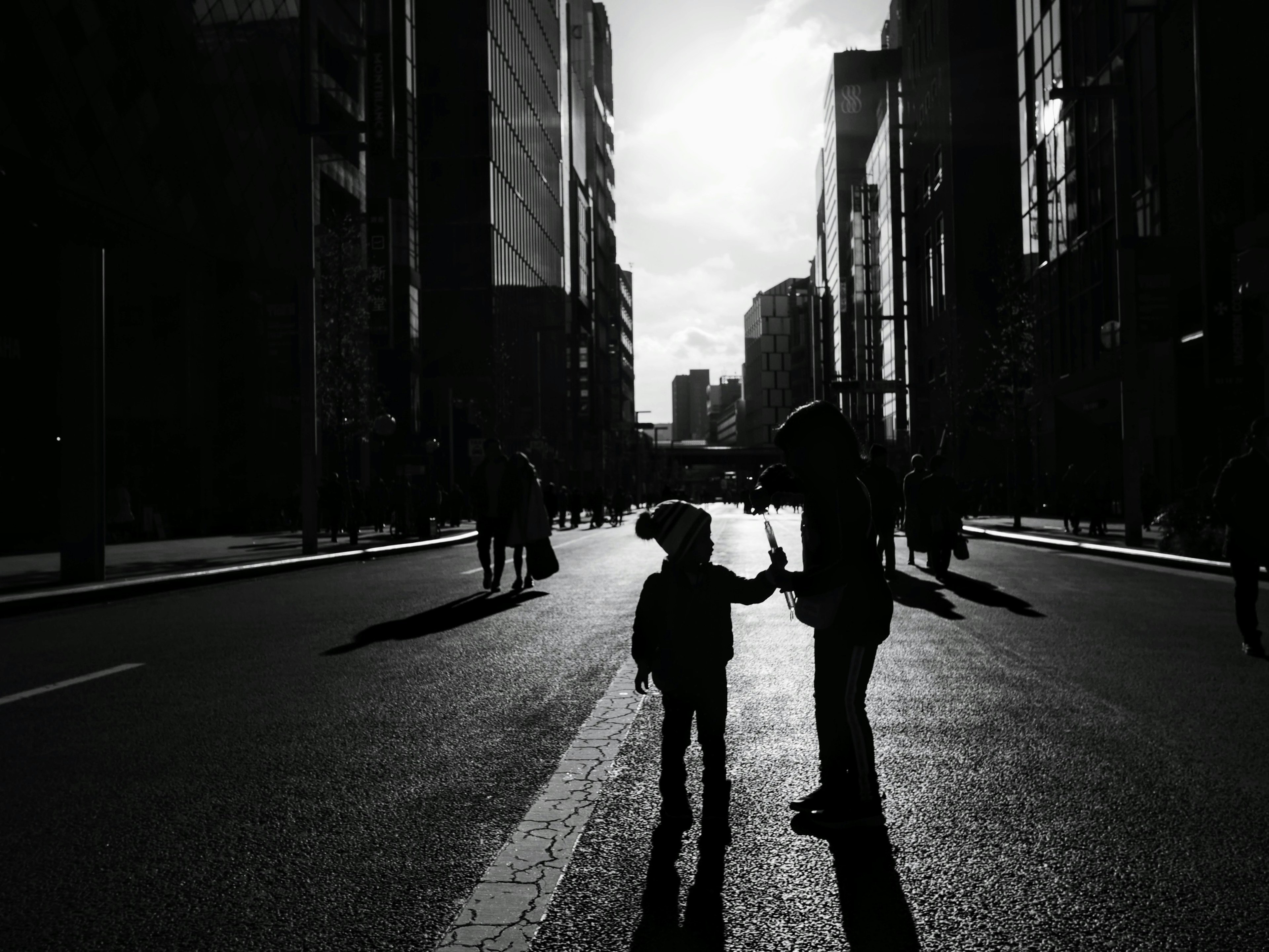 Silhouette of a child and adult holding hands in a city street