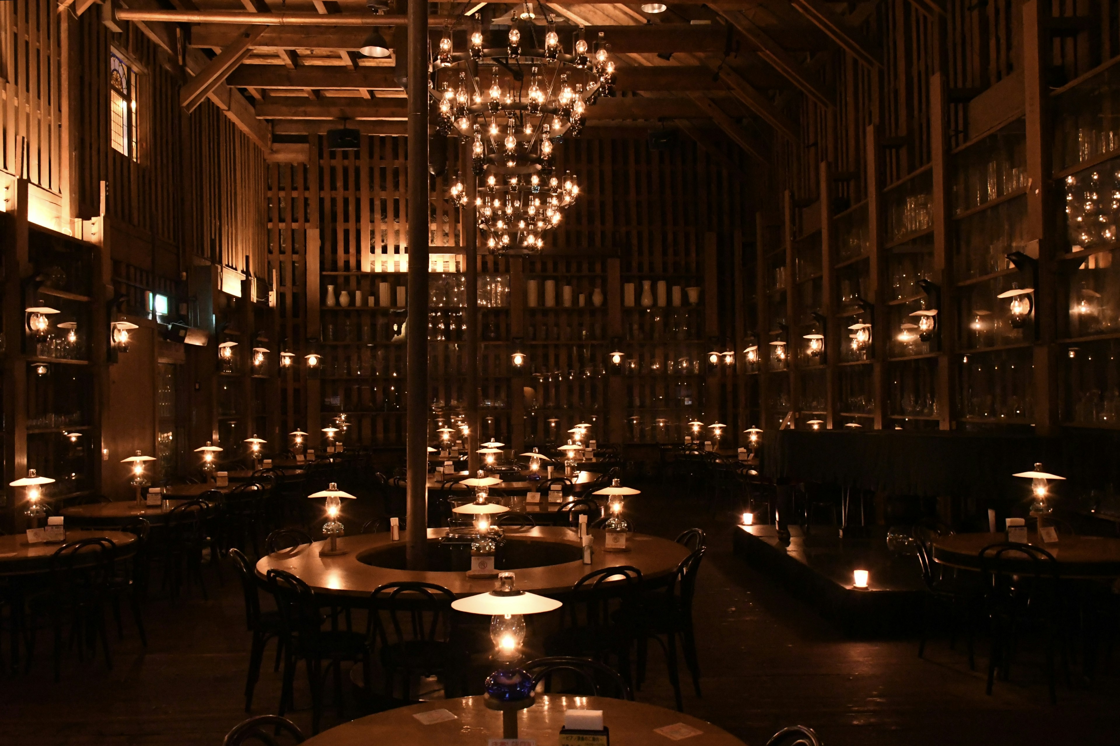 Interior of a dimly lit restaurant featuring a large chandelier and numerous tables