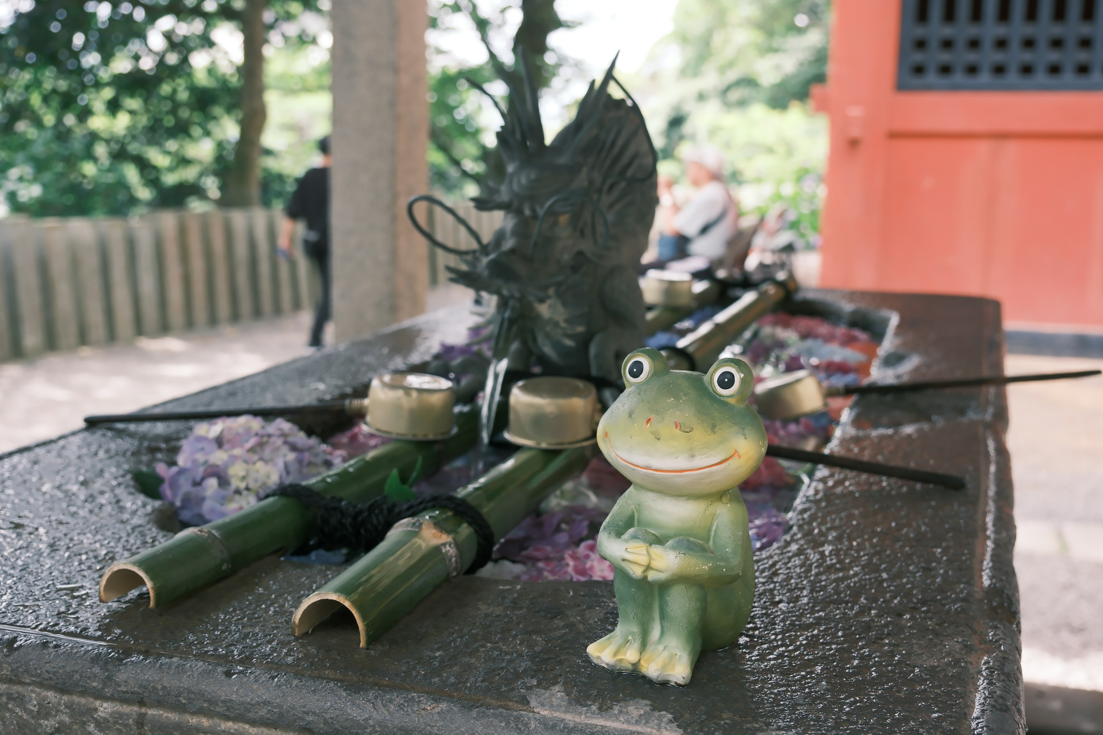 Una figura de rana junto a decoraciones de bambú y piedra en un entorno verde al aire libre