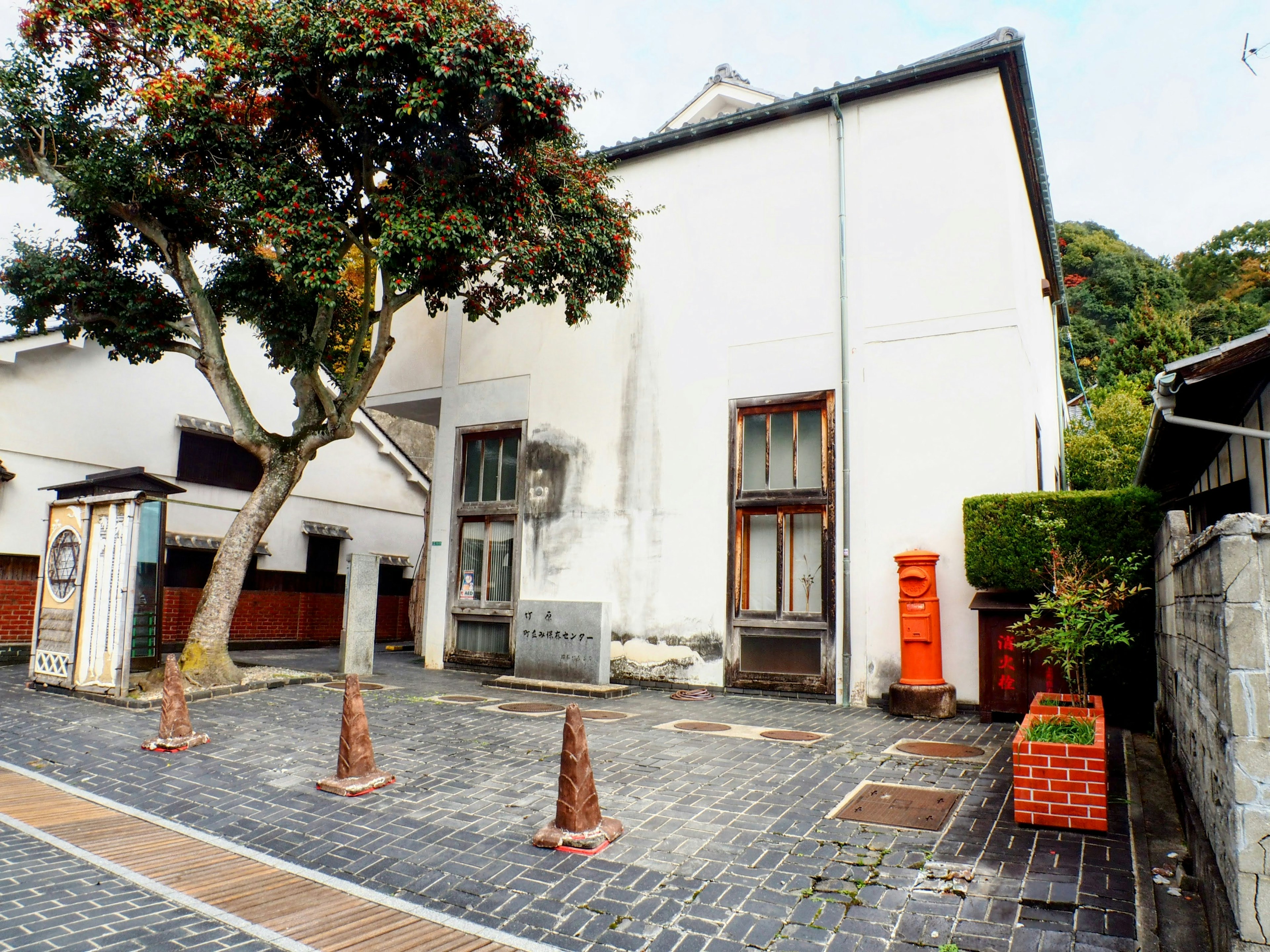 Quiet street scene featuring a white building and green tree Red mailbox and cobblestone path are prominent