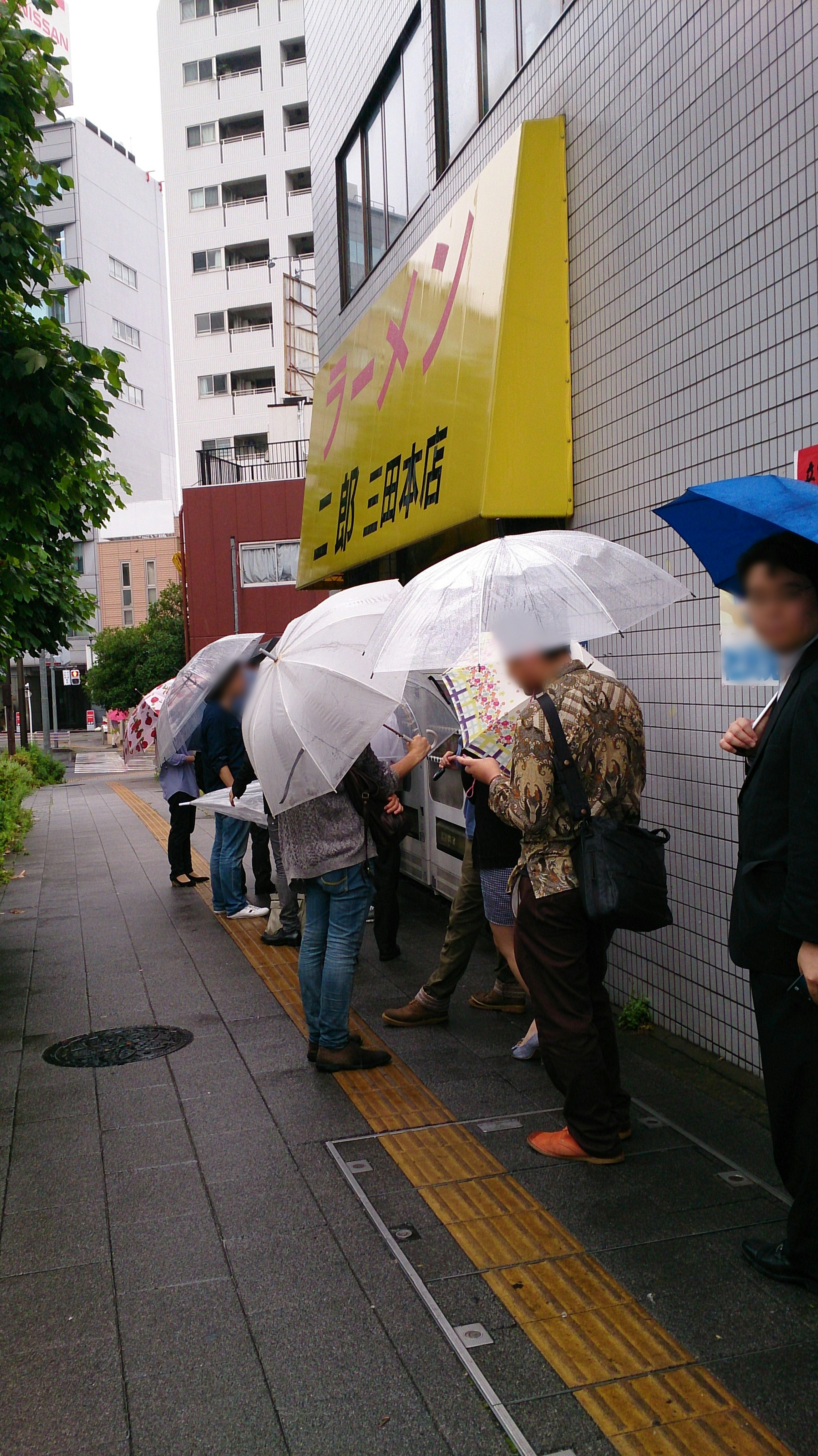 人々が傘をさして並んでいる風景 屋根のある店舗の前