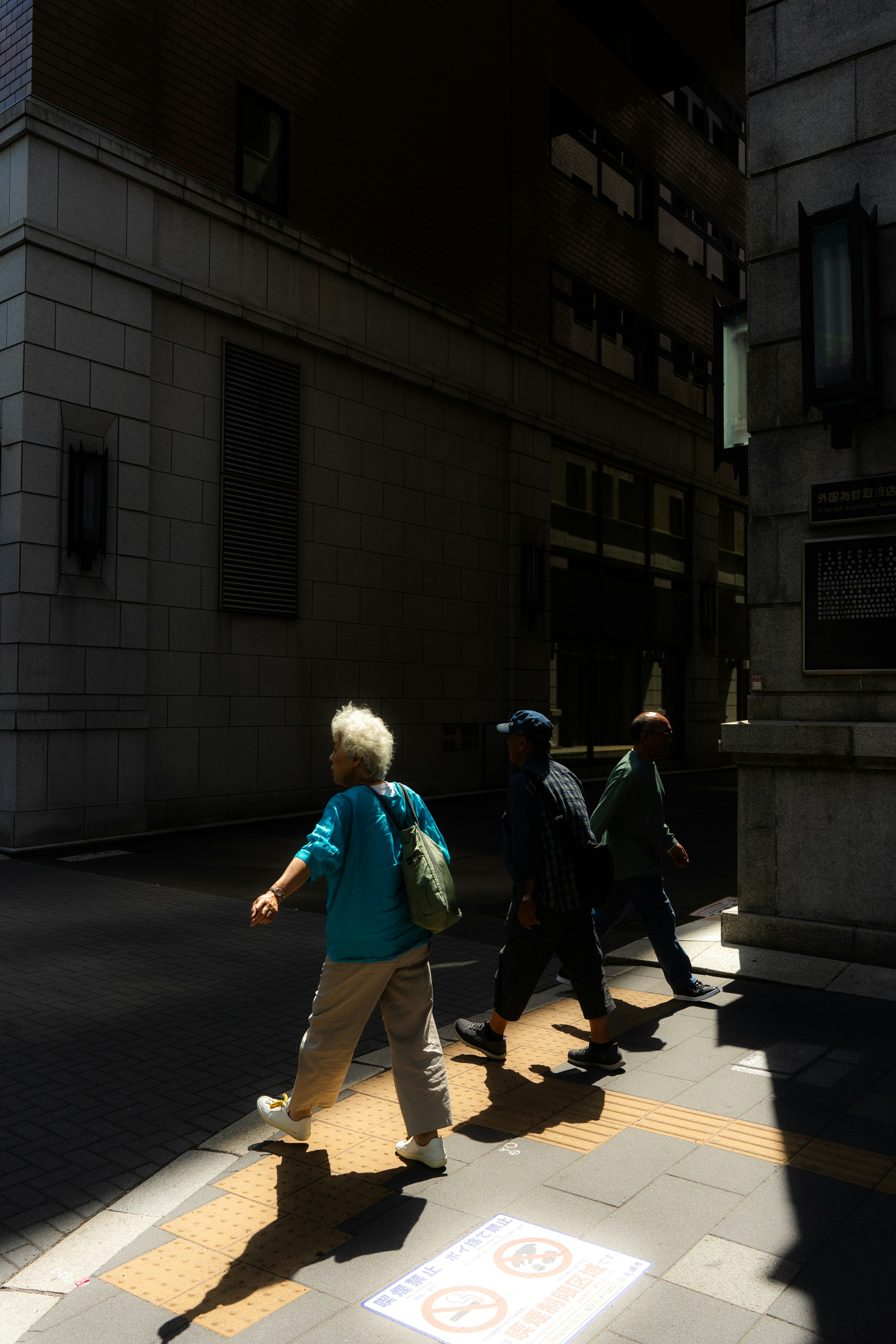 Siluetas de personas caminando a la luz del sol una persona mayor con una camisa azul y otras dos fuerte contraste de sombras