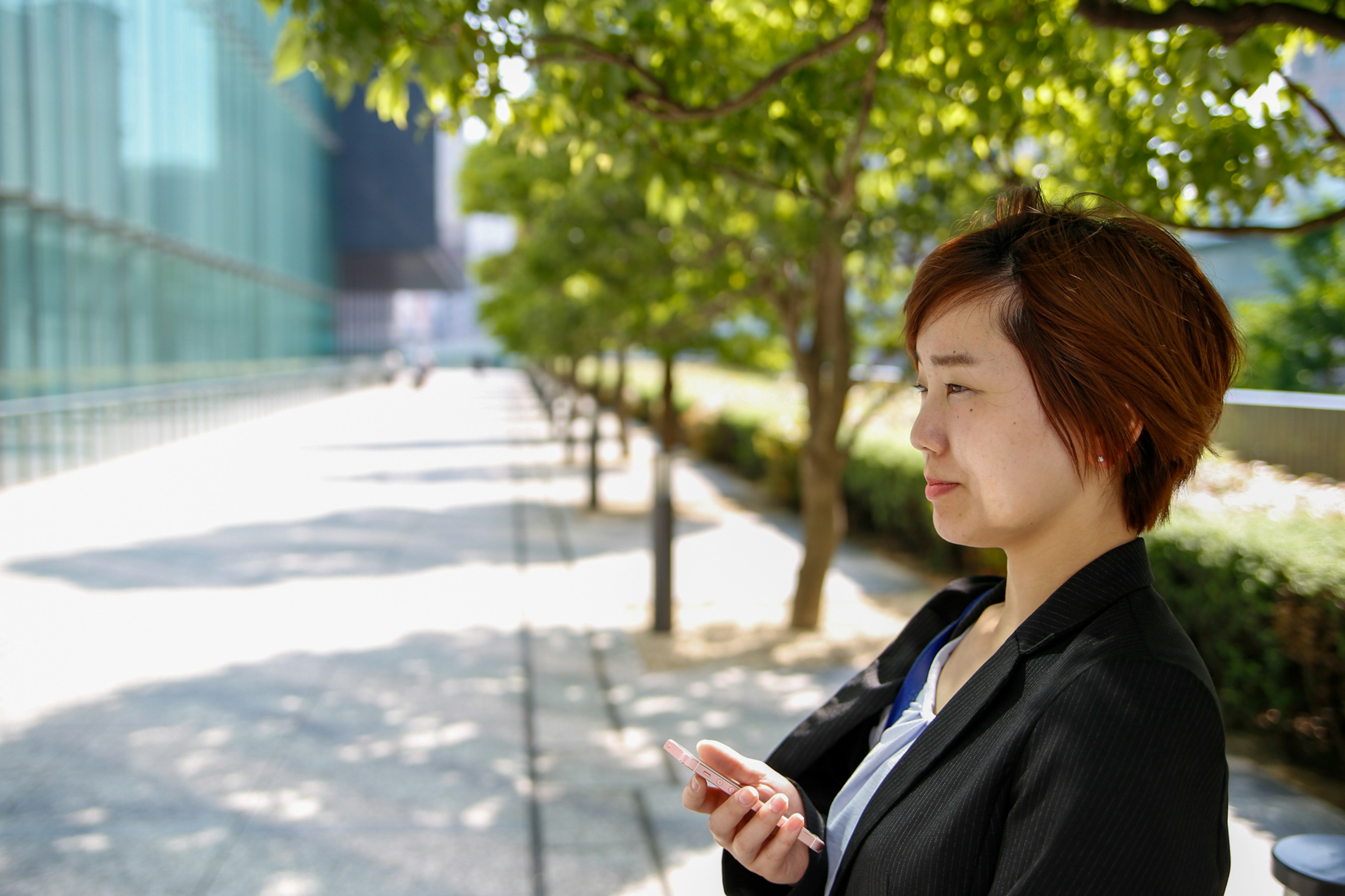 A woman in a suit deep in thought on a city street surrounded by green trees